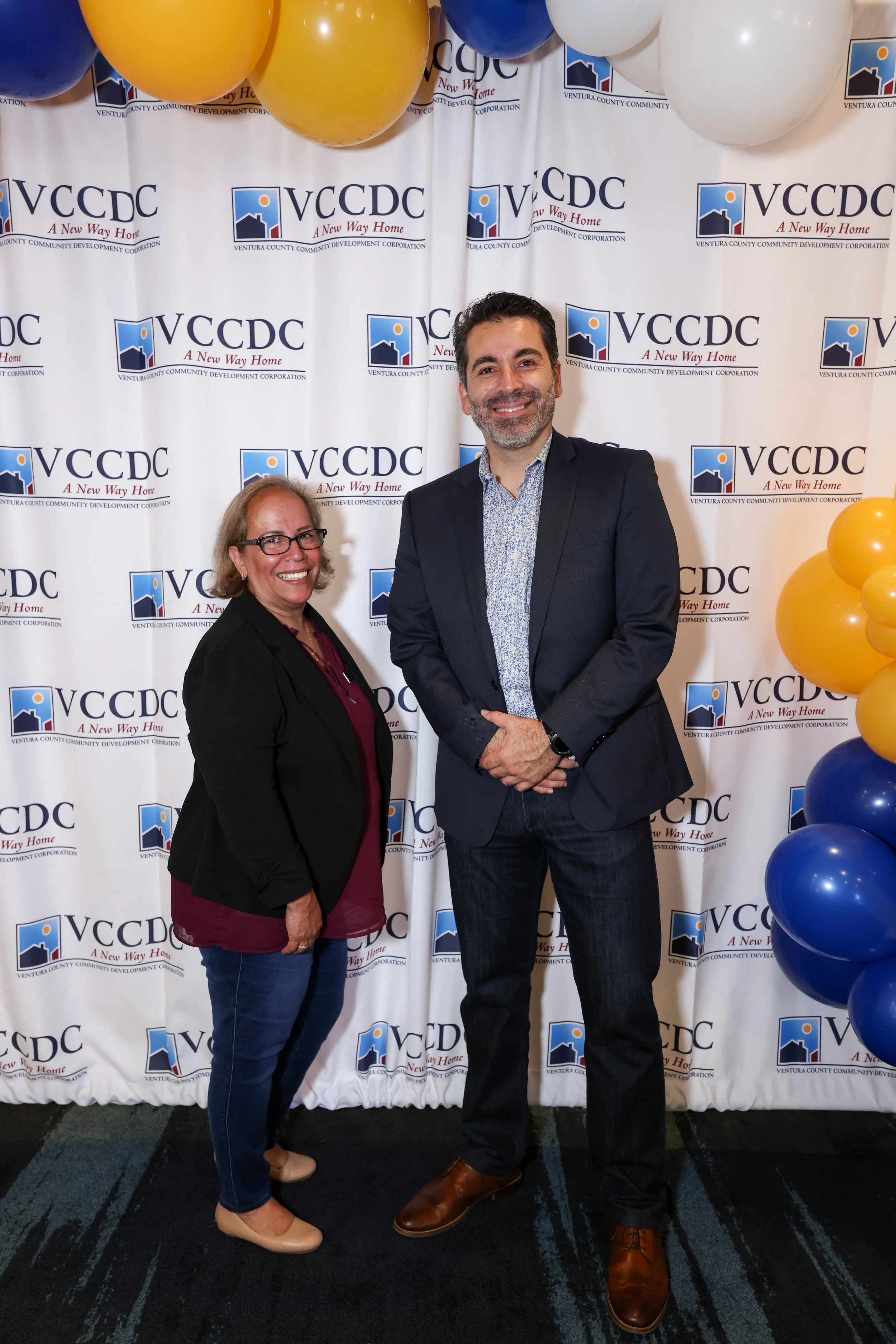 Man and woman in front of photo backdrop at indoor community event