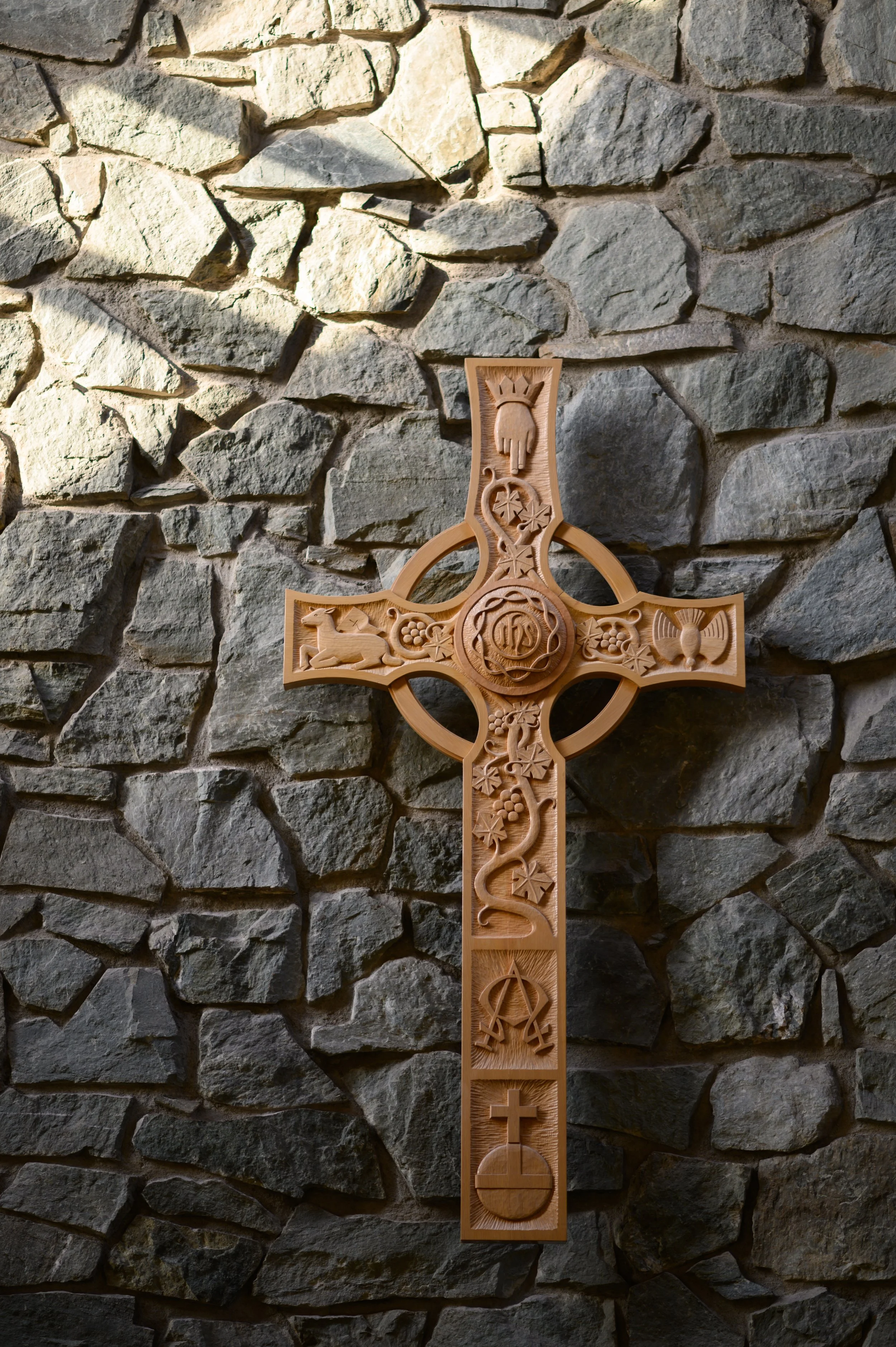 Wooden Celtic cross with intricate carvings and symbols, mounted on a stone wall.