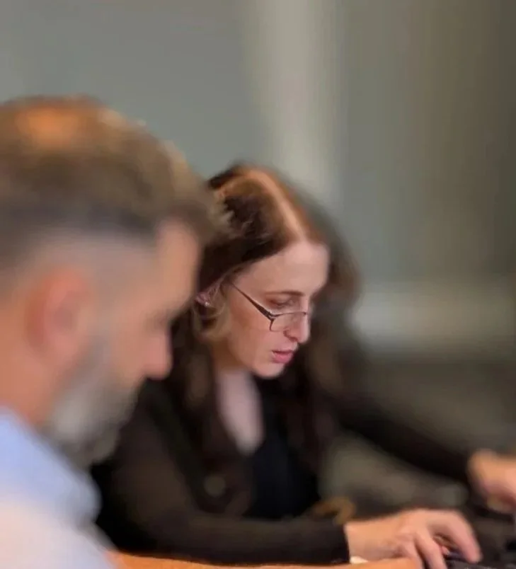Two individuals sitting at a desk, working on laptops in a professional setting.