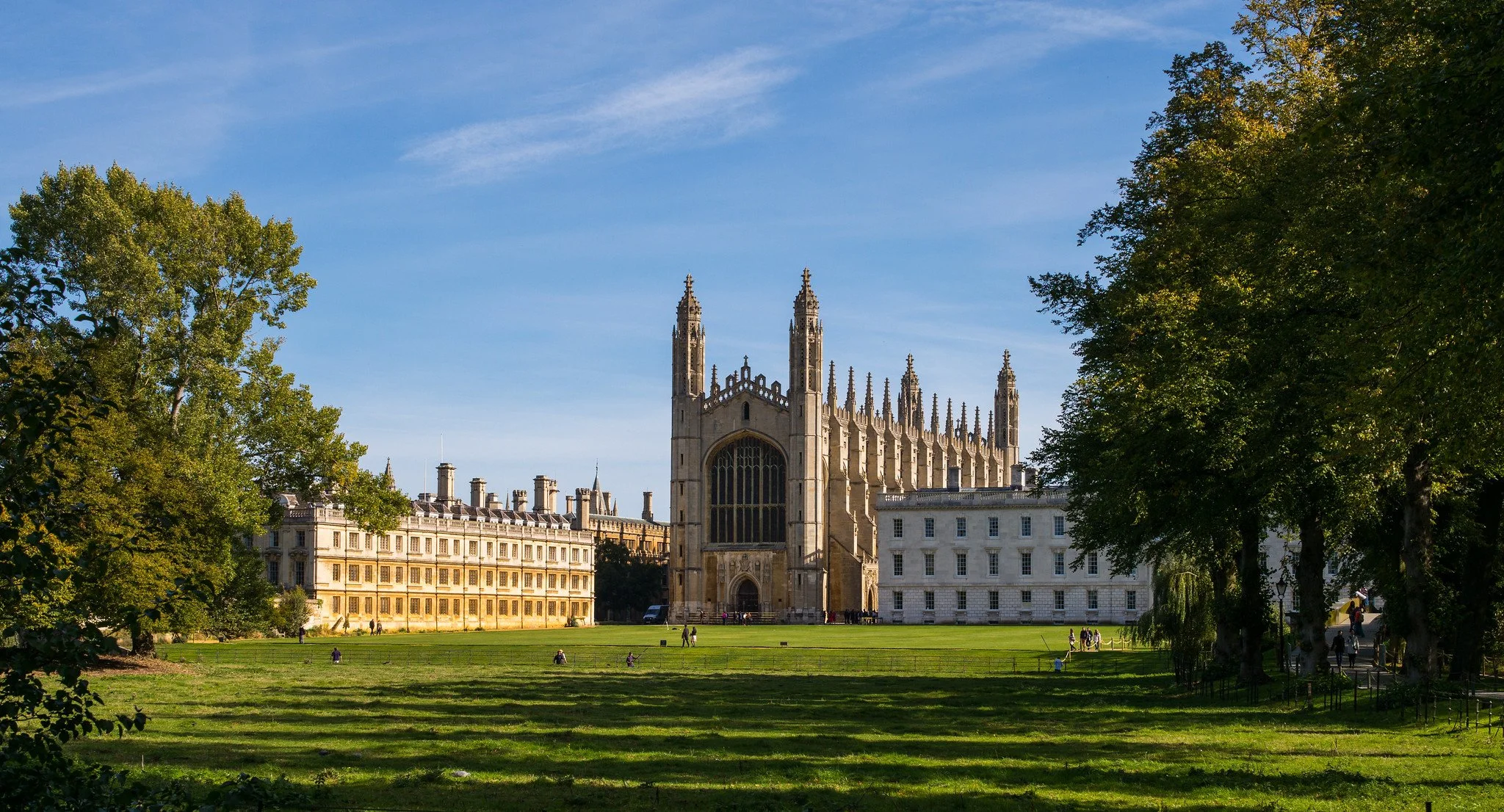 A historic cathedral with tall spires and large stained glass window, surrounded by trees and green lawn in a park setting.