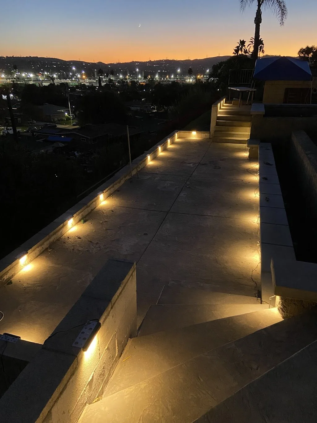 Outdoor pathway with ground lights at dusk overlooking cityscape and sunset sky
