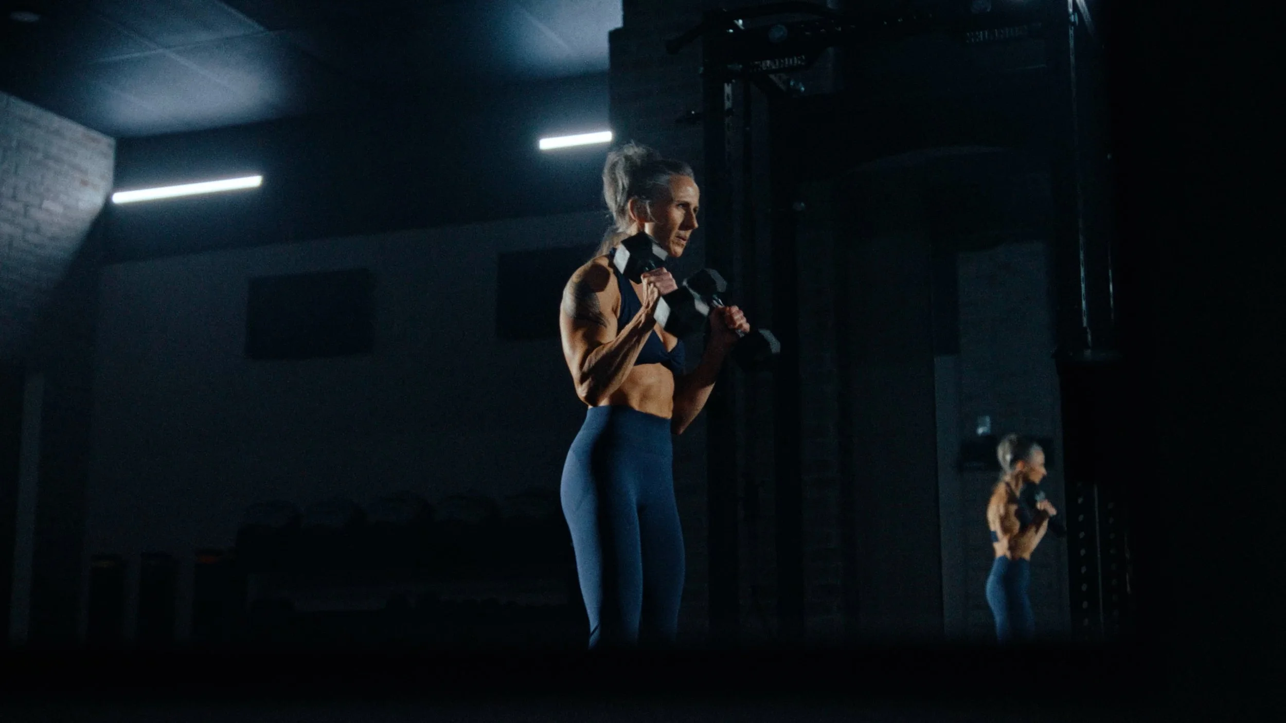 workout commercial solin fitness creator Cheryl Coulombe lifting dumbbells in dark moody gym 