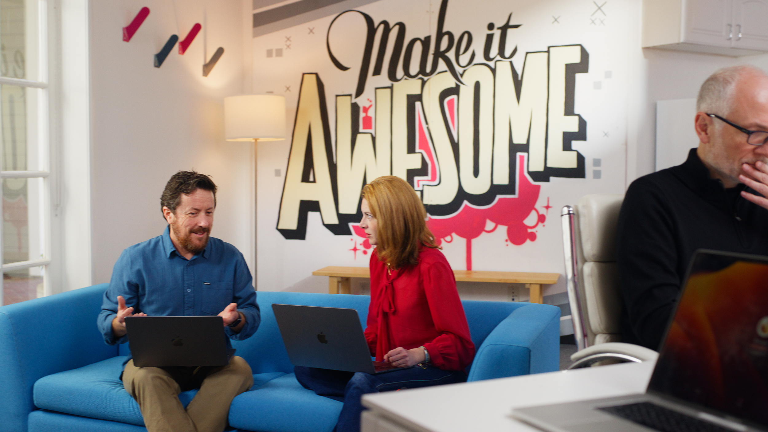 Office space with desks, chairs, and equipment, lit with a mix of natural and artificial light, with the words 'Together We' overlayed in pink and white. Screenshot from an advertising video for Kiosk marketing agency.