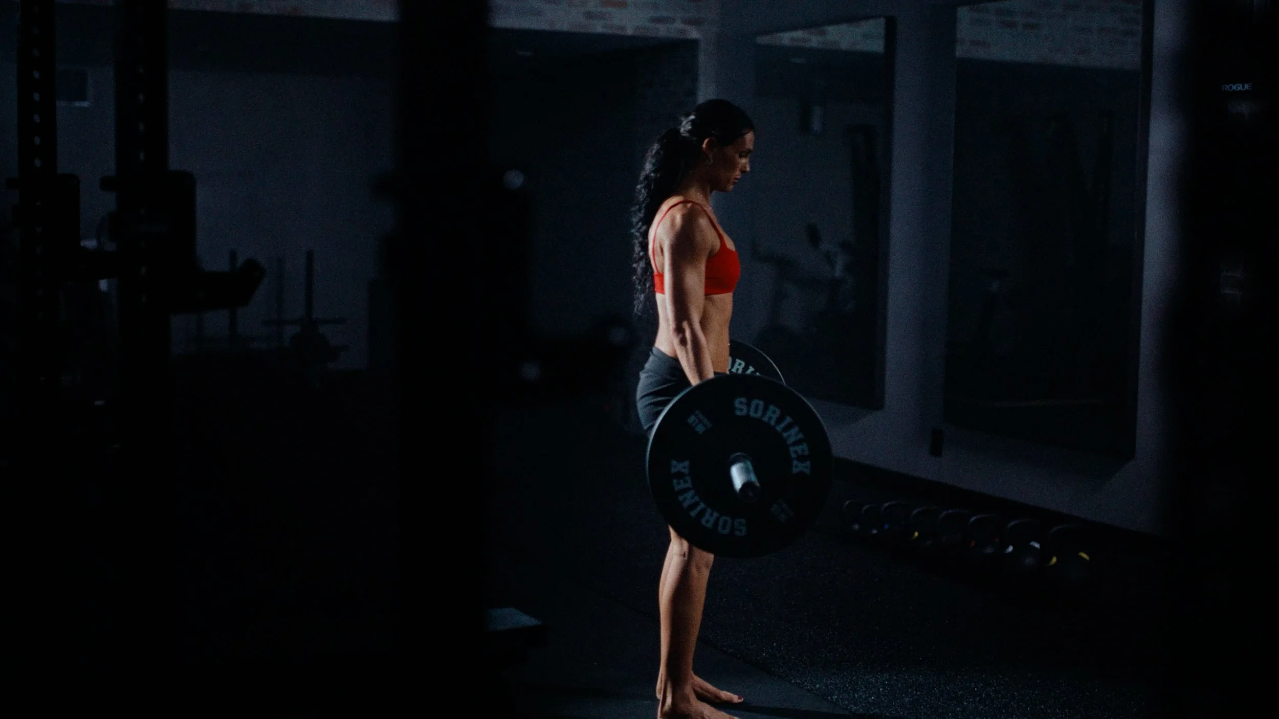 workout commercial solin fitness creator Anna McClellan lifting weights in dark moody gym 