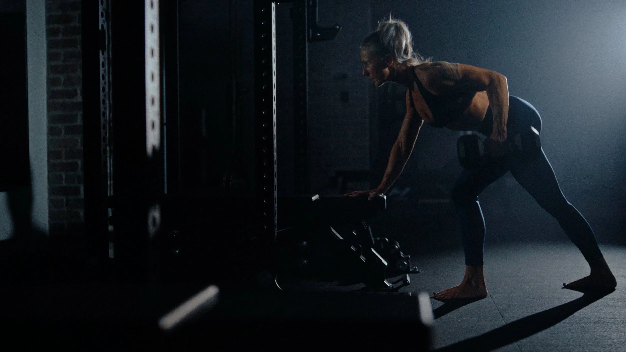 workout commercial solin fitness creator Cheryl Coulombe lifting weights in dark moody gym 