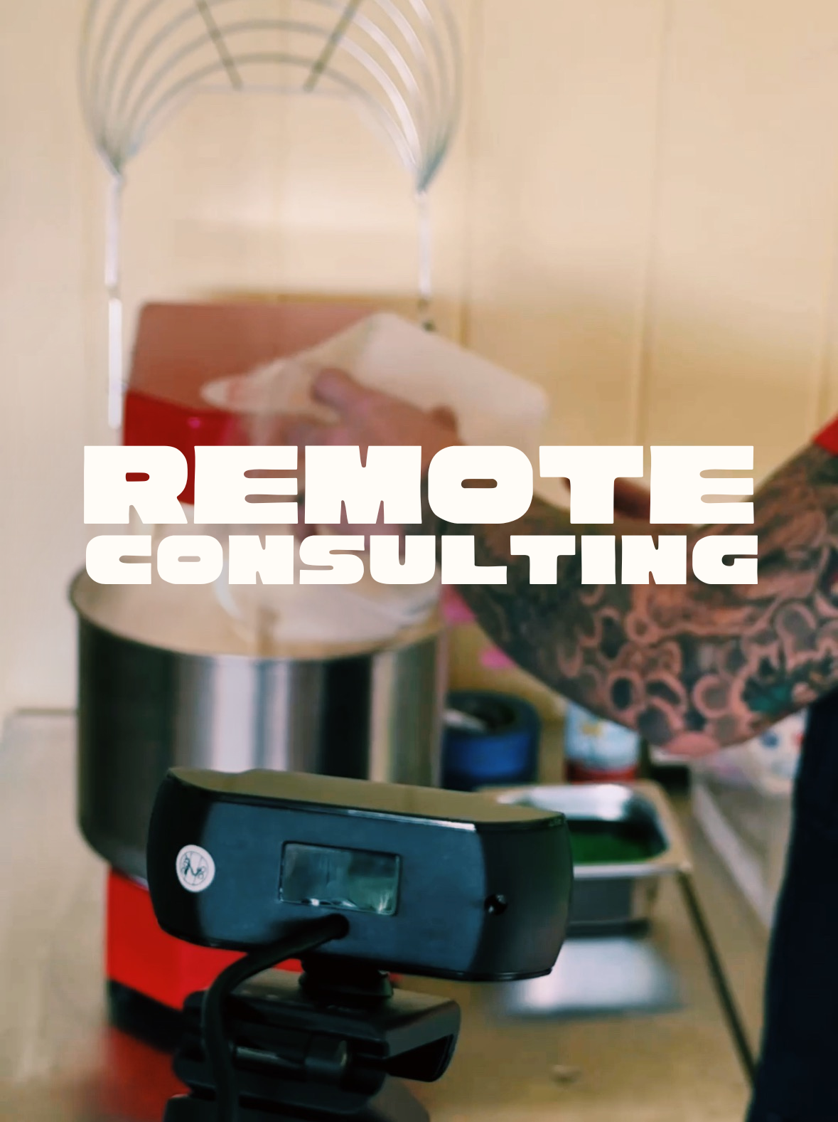 Pizza consultant Alastair Hannmann Al the Pizza Buddha mixing dough ingredients into a spiral dough mixer, with a remote consulting camera in the foreground and bold text overlay that says 'REMOTE CONSULTING.'
