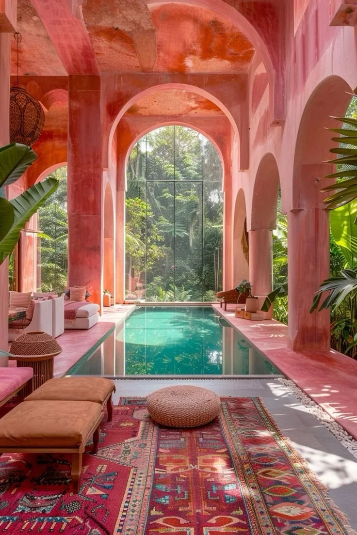 Indoor pool area with pink arches, tropical plants, and large window showcasing greenery outside.