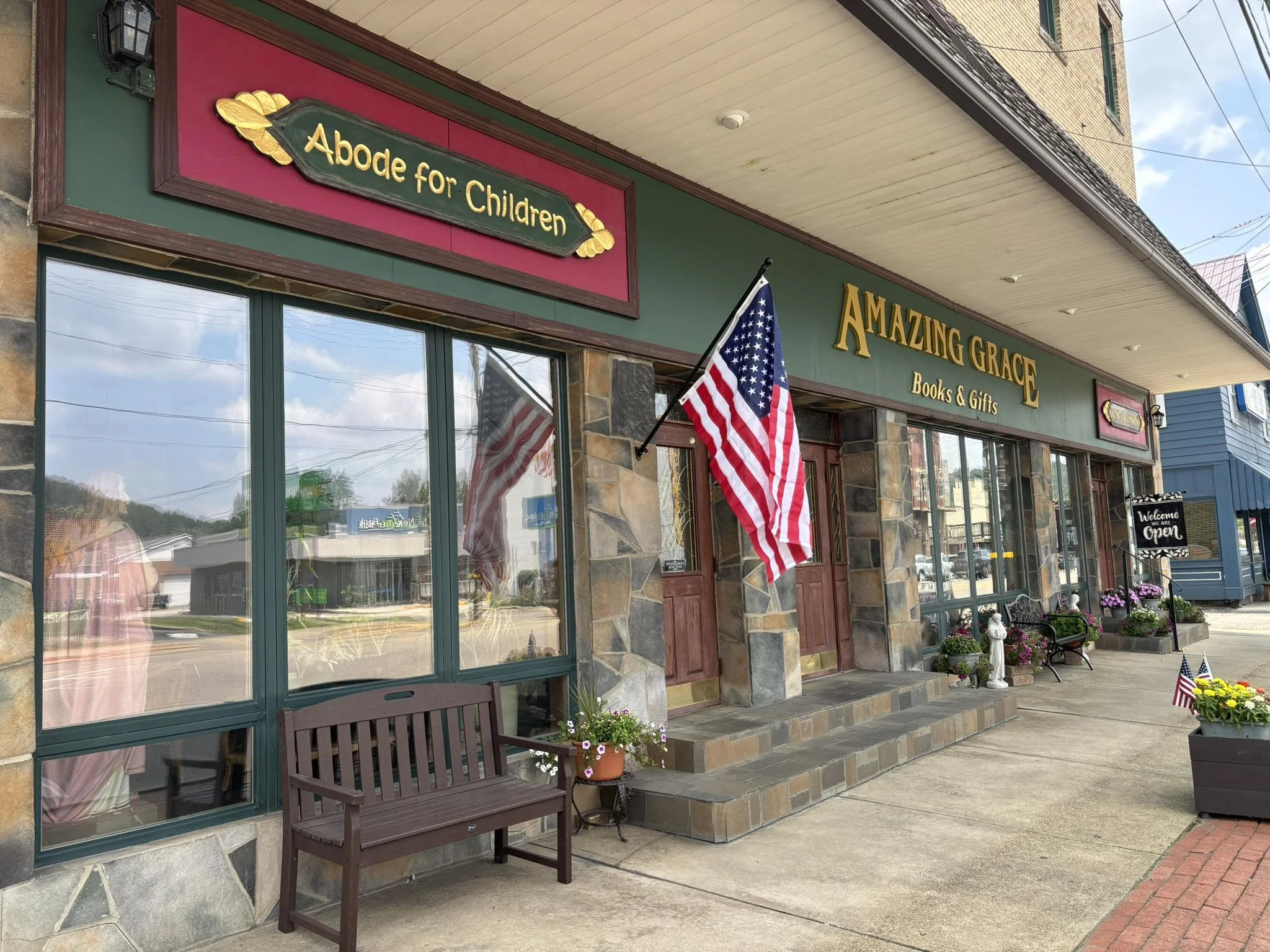 Storefront of Amazing Grace Books & Gifts with Abode for Children sign, displaying a stone facade and festive string lights in a commercial building.