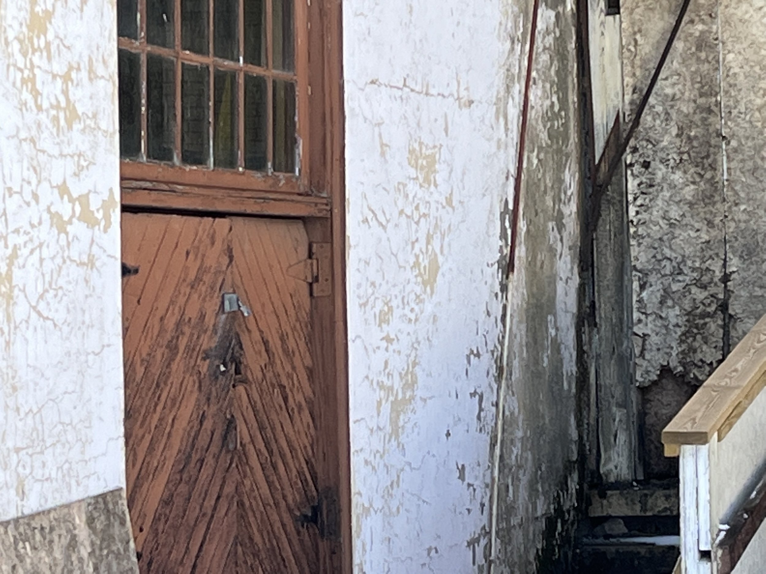Weathered wooden door with glass panes, chipped paint on surrounding walls, and narrow staircase in rustic setting.