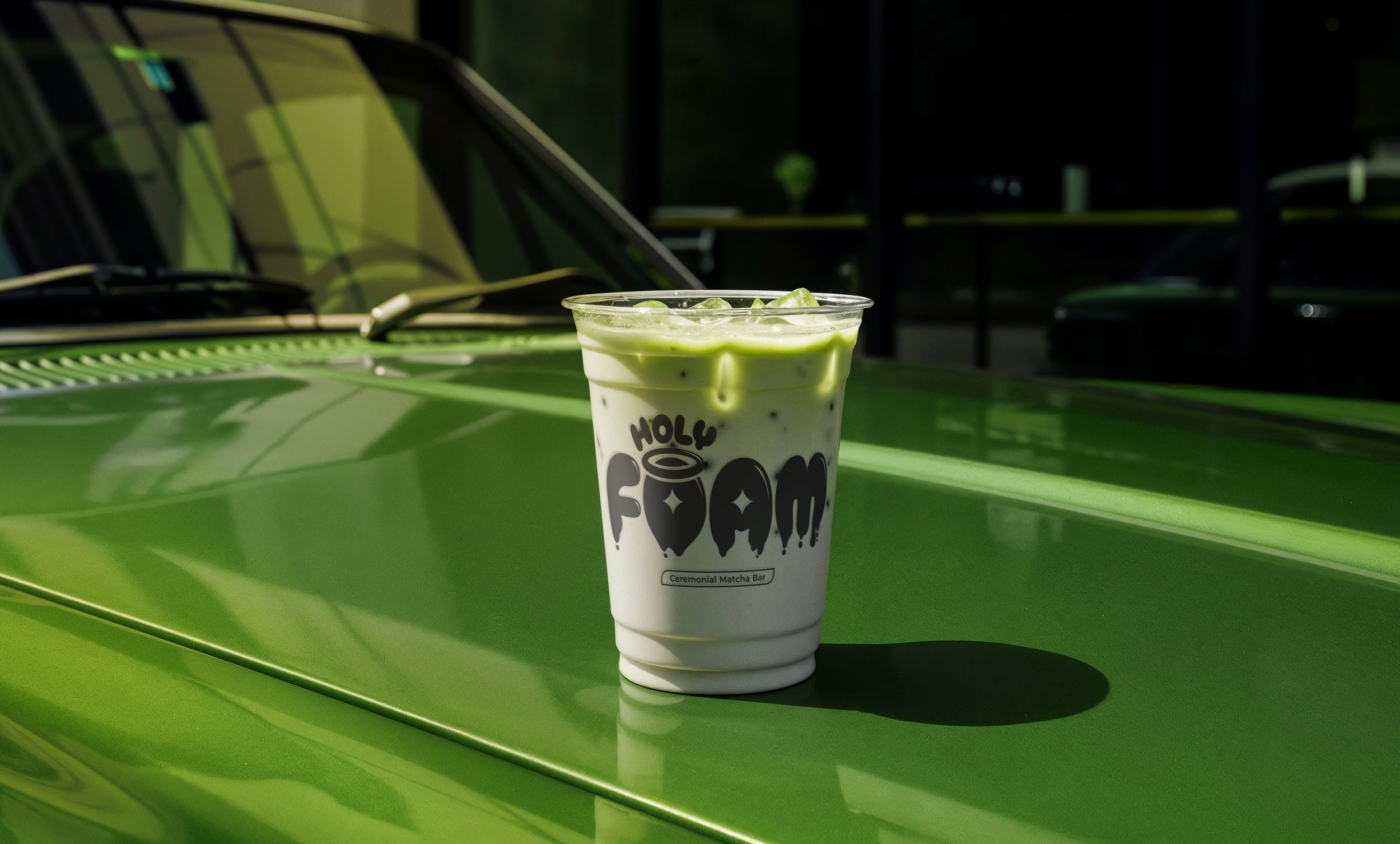 Vaso de bebida verde y blanca con hielo y un logo que dice 'Holy Foam' sobre un auto verde.