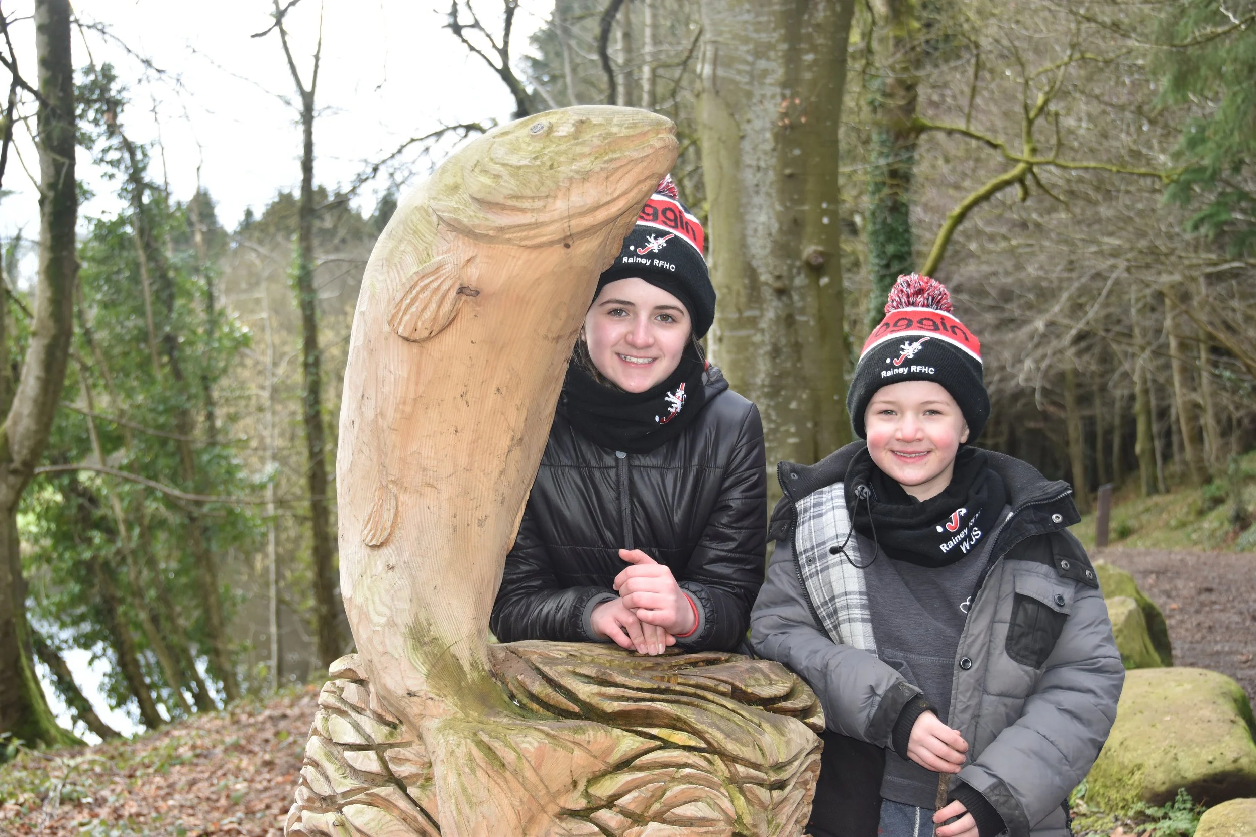 Two young people beside a carved wooden fish sculpture on a woodland walk
