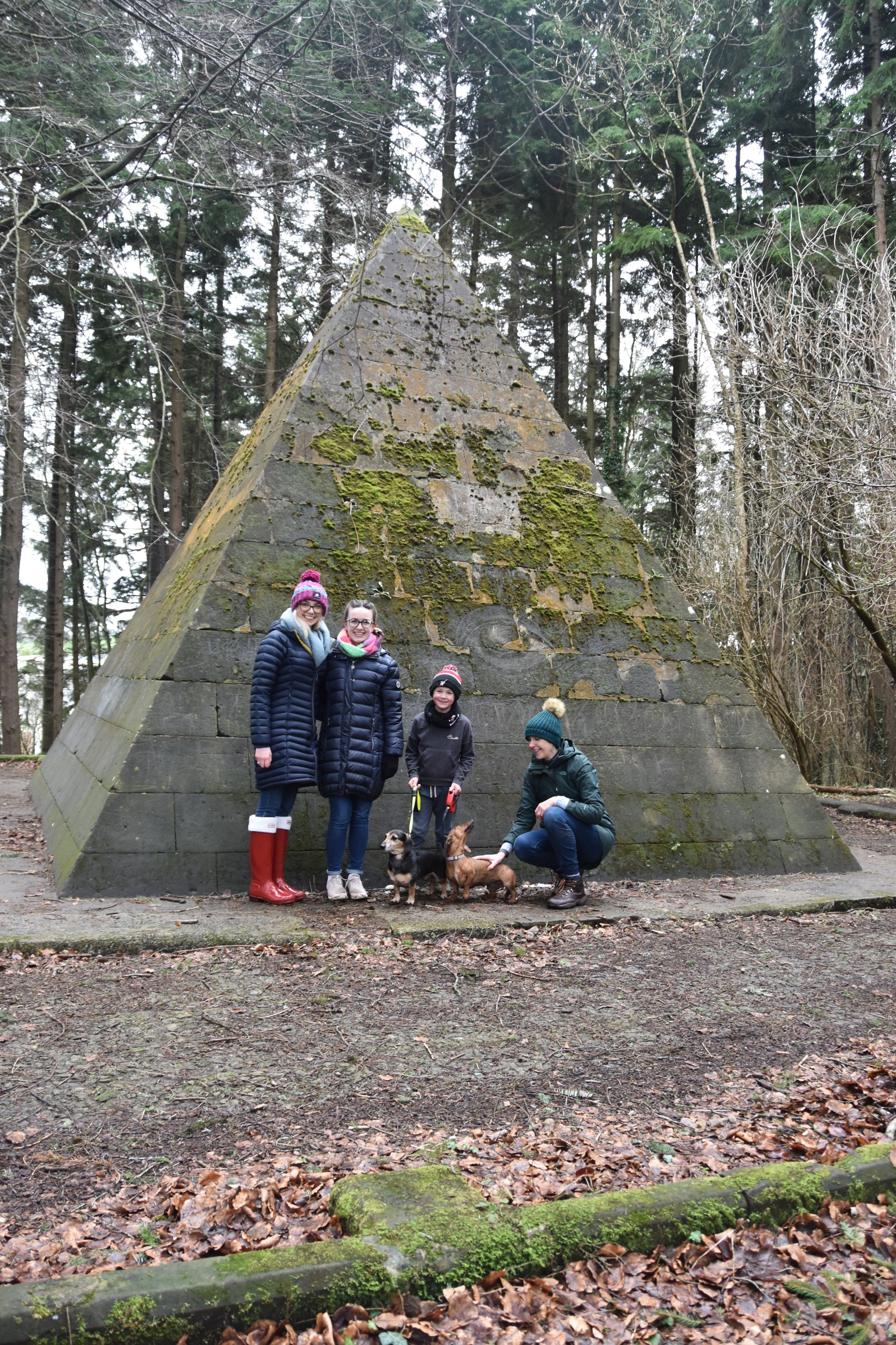 Young people and a dog beside a stone pyramid monument in the woods