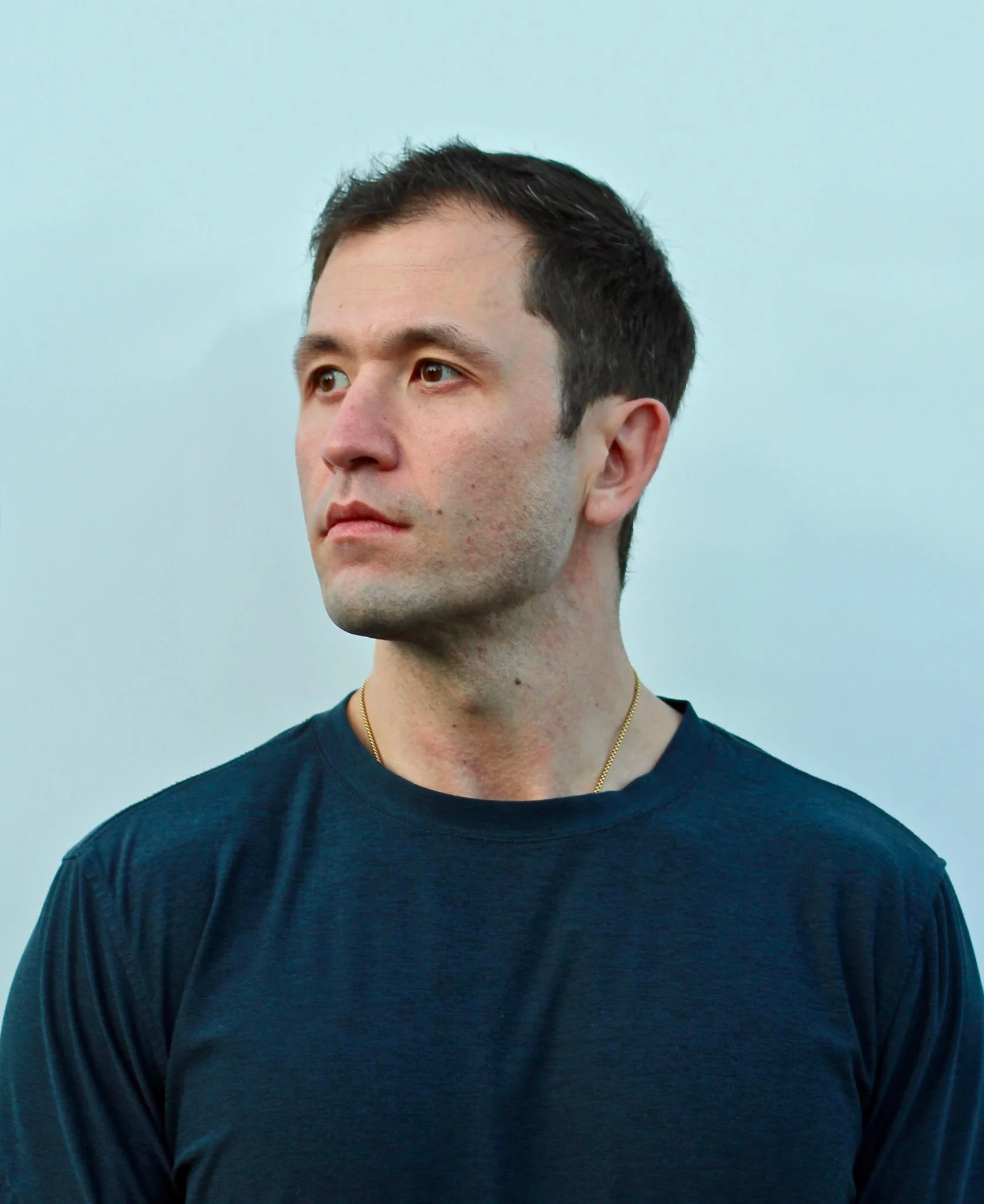 Man in a dark blue shirt looking to the left against a plain background.