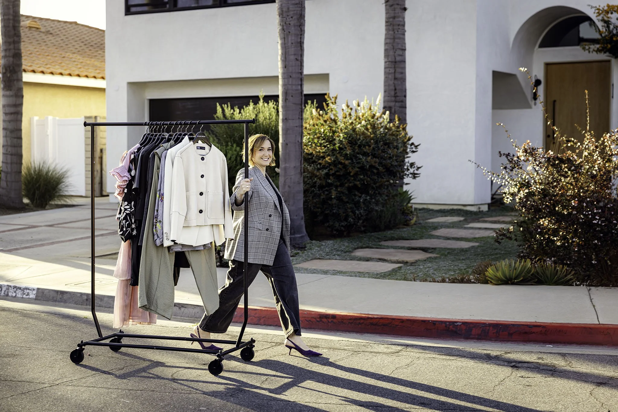 Heather Chee, Orange County personal stylist and founder of Stylized Threads, rolling a clothing rack down a sunny residential street in a plaid blazer — lifestyle branding photography by Vera Gosic, Long Beach
