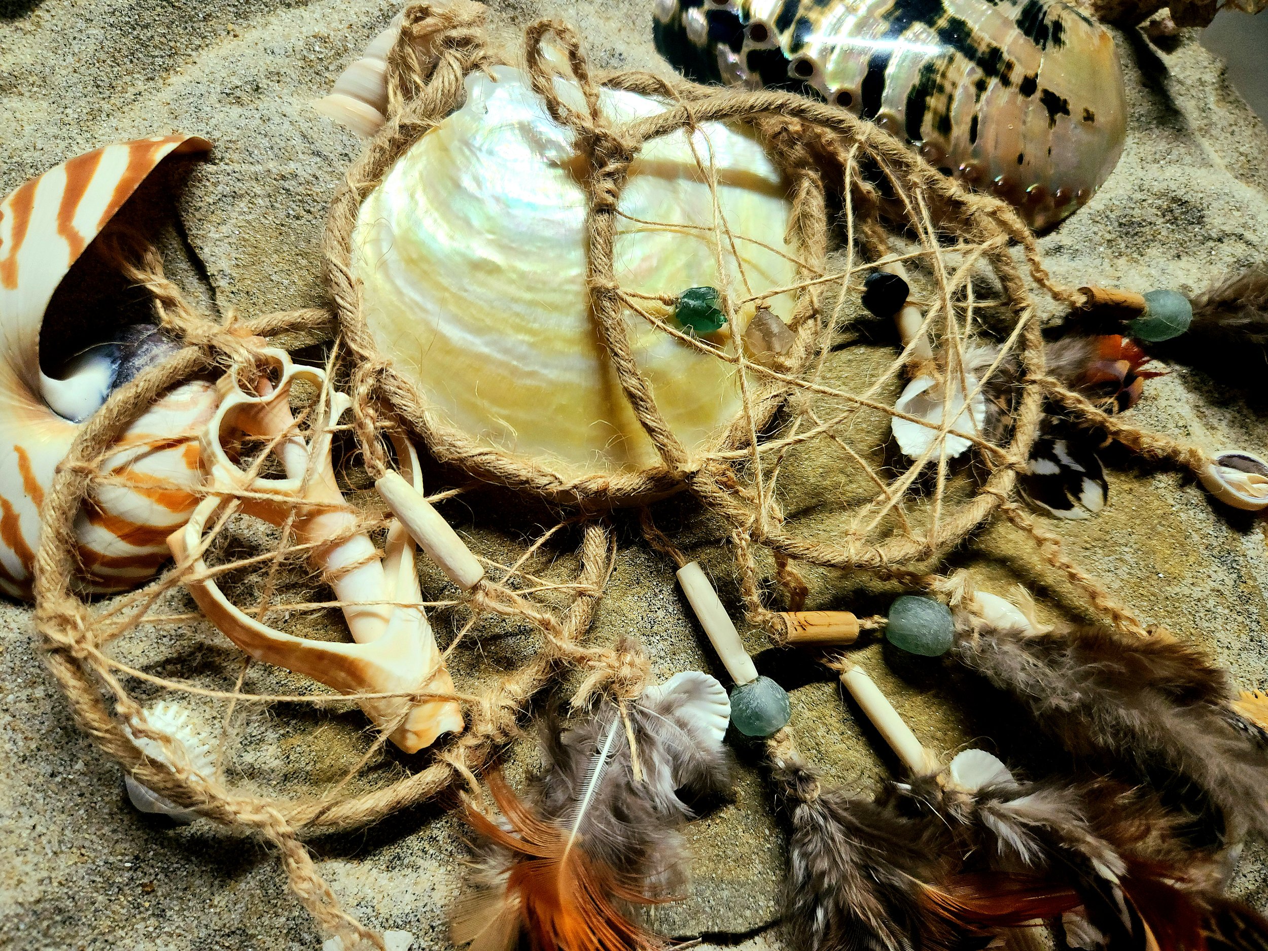 Various seashells, feathers, beads, and a wrapped shell on sandy surface.