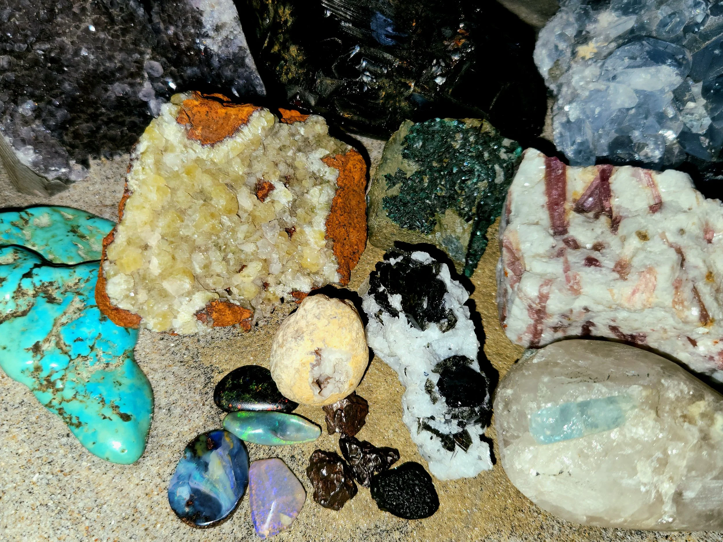 Collection of various colorful rocks and minerals on a sandy surface