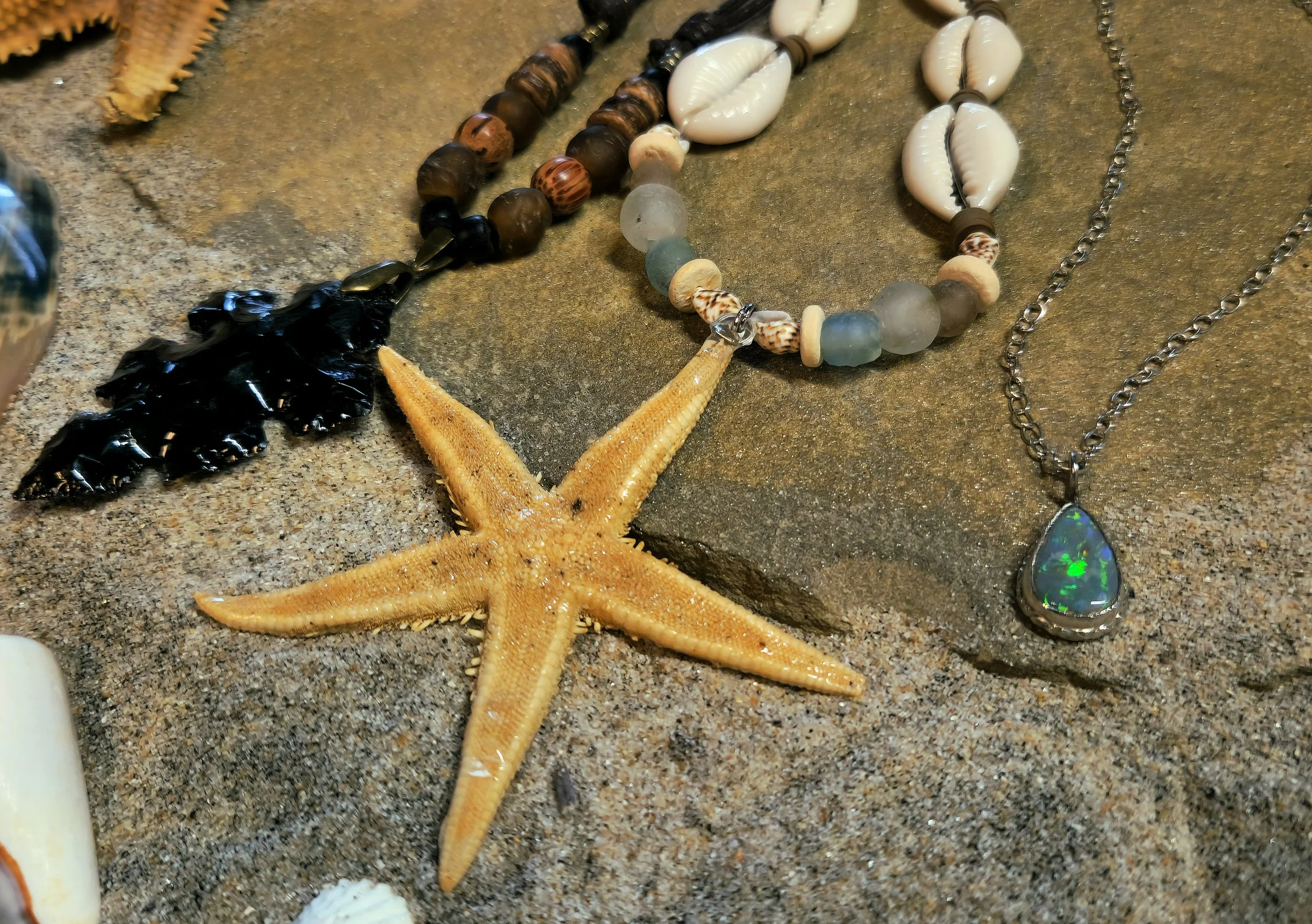 Various seashells and a starfish on a sandy surface, with some jewelry including necklaces and a pendant.