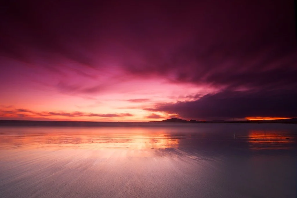 Colorful sunset over a calm body of water with a mountain silhouette in the distance.
