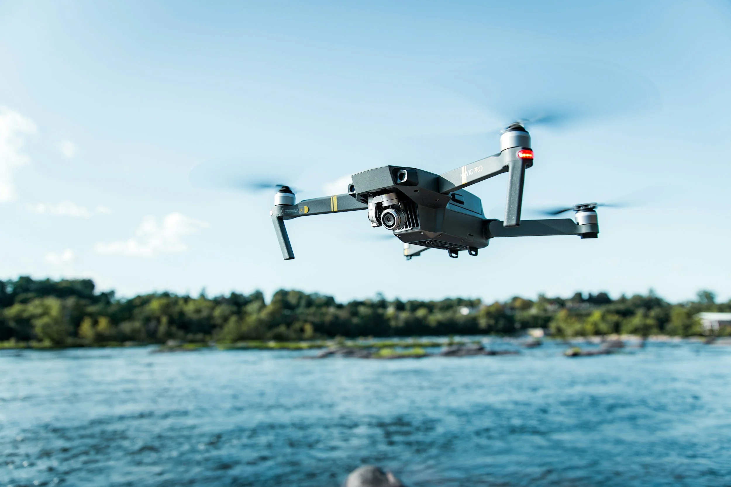 A drone flying over a body of water with trees in the background on a clear day.