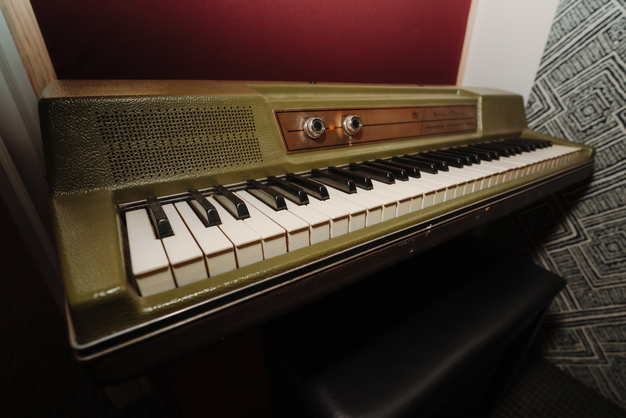 Vintage green keyboard with black and white keys and two control knobs on a wooden surface, against a red and patterned background.