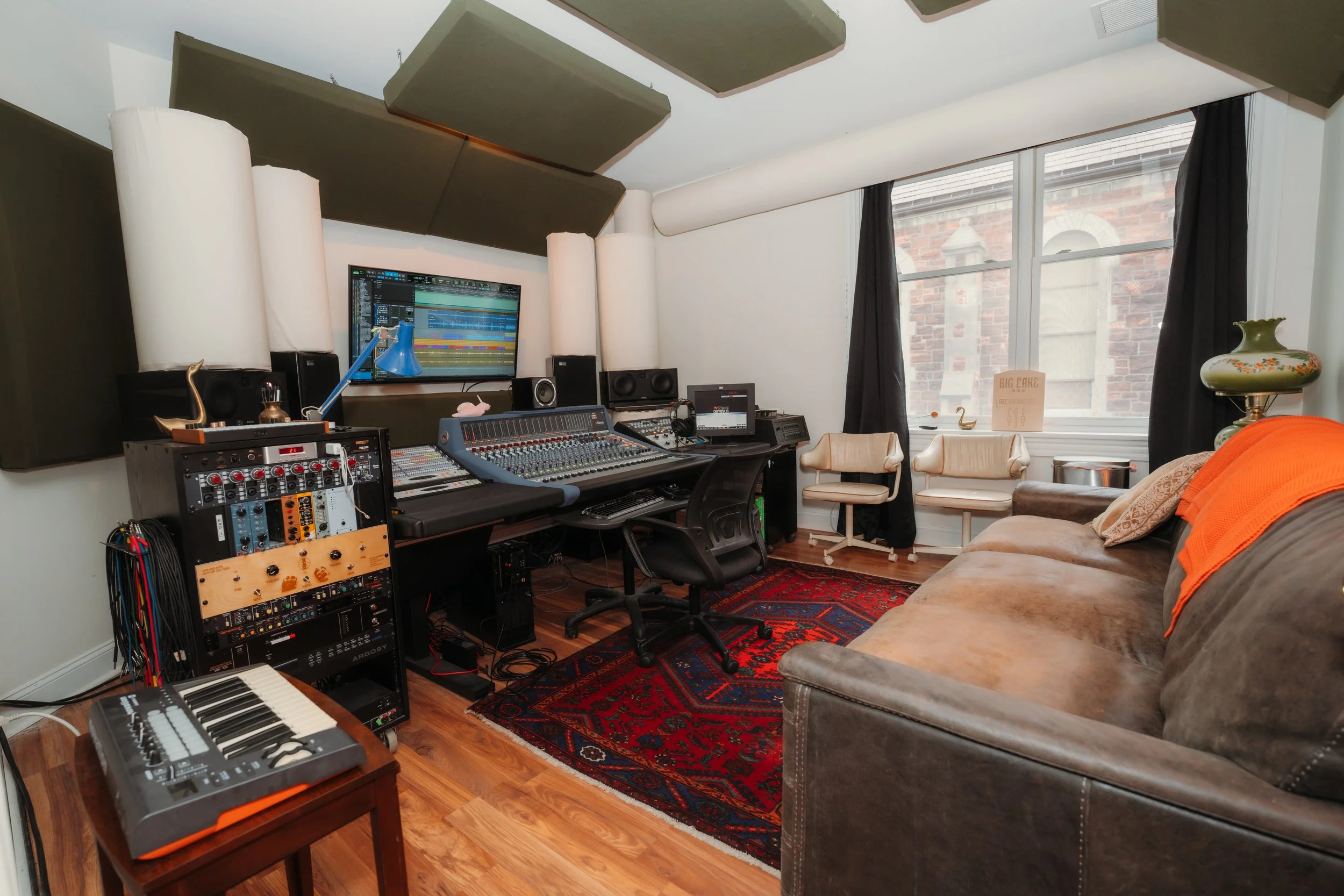 Music recording studio with mixing console, computer screens, musical equipment, and seating area with sofa and chairs.
