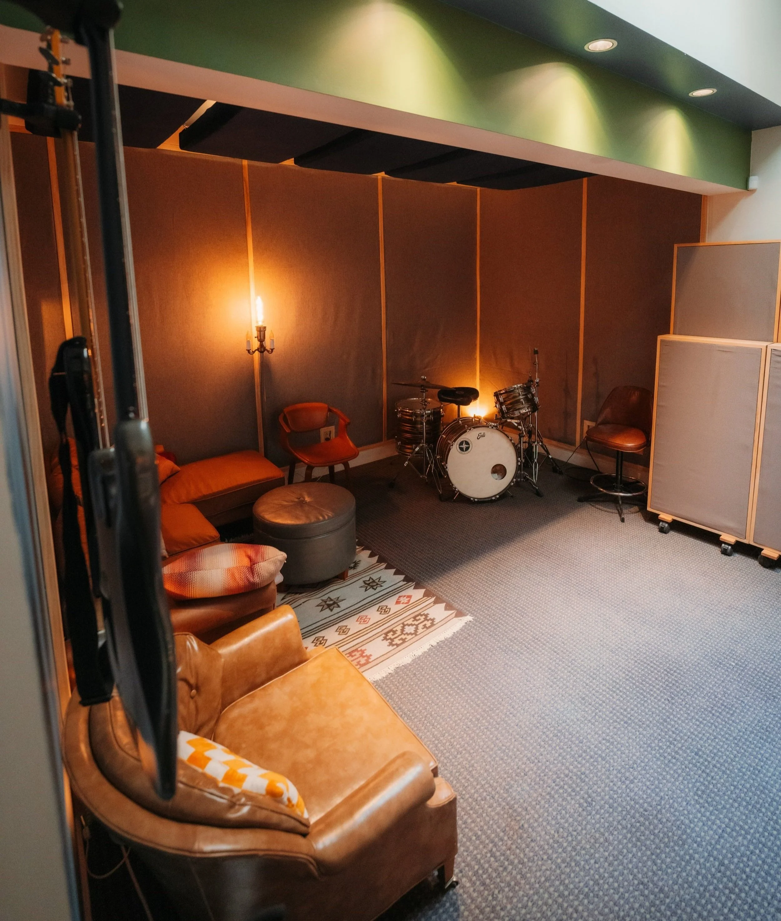 A cozy music recording studio with a drum set, seating, and soundproofing panels.