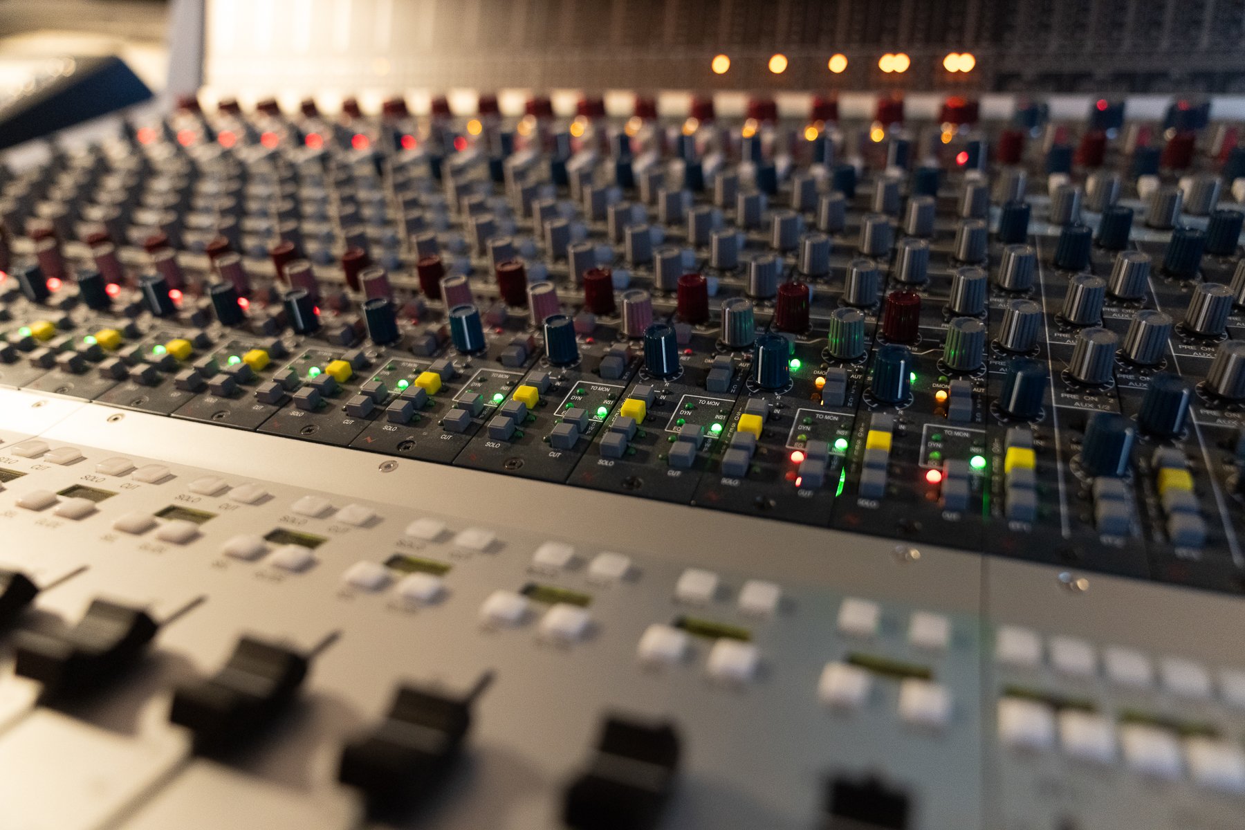 Close-up of an audio mixing console with numerous colorful knobs, buttons, and sliders.