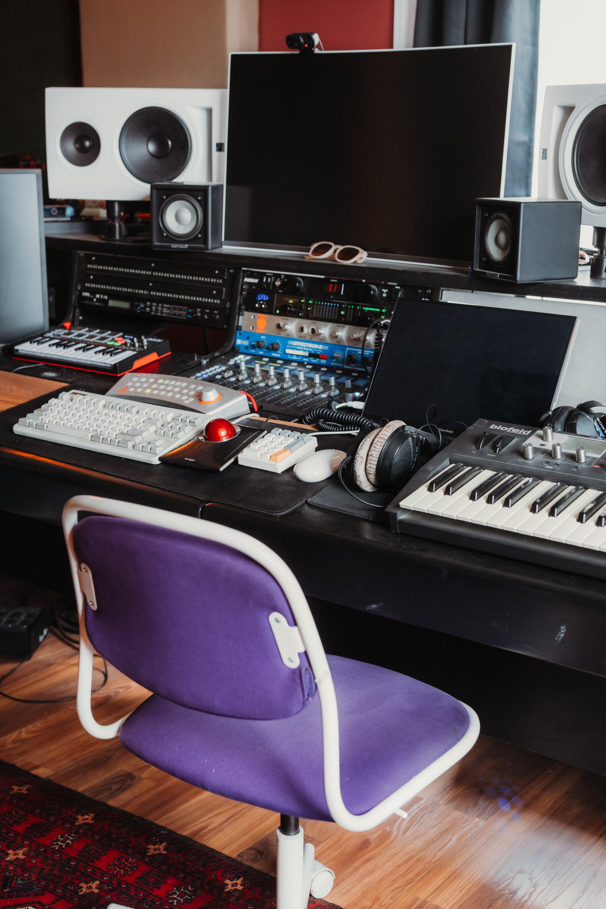 Music production studio setup with computer monitors, studio speakers, audio equipment, a keyboard, and a purple office chair.