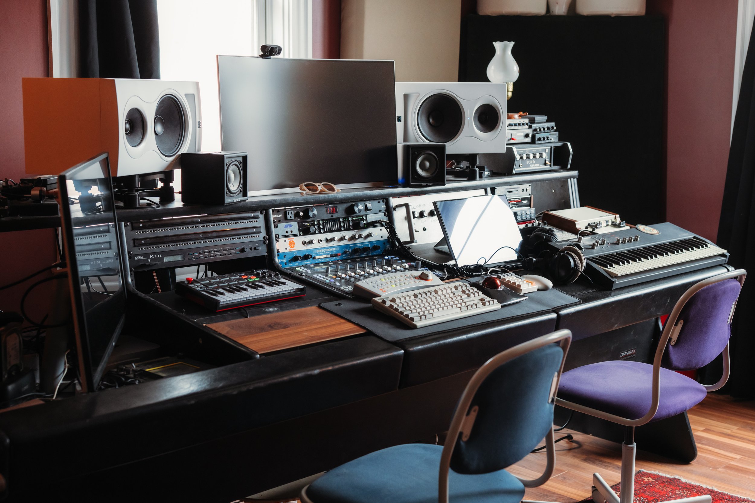 Music production studio with computers, audio equipment, studio monitors, keyboard, and headphones
