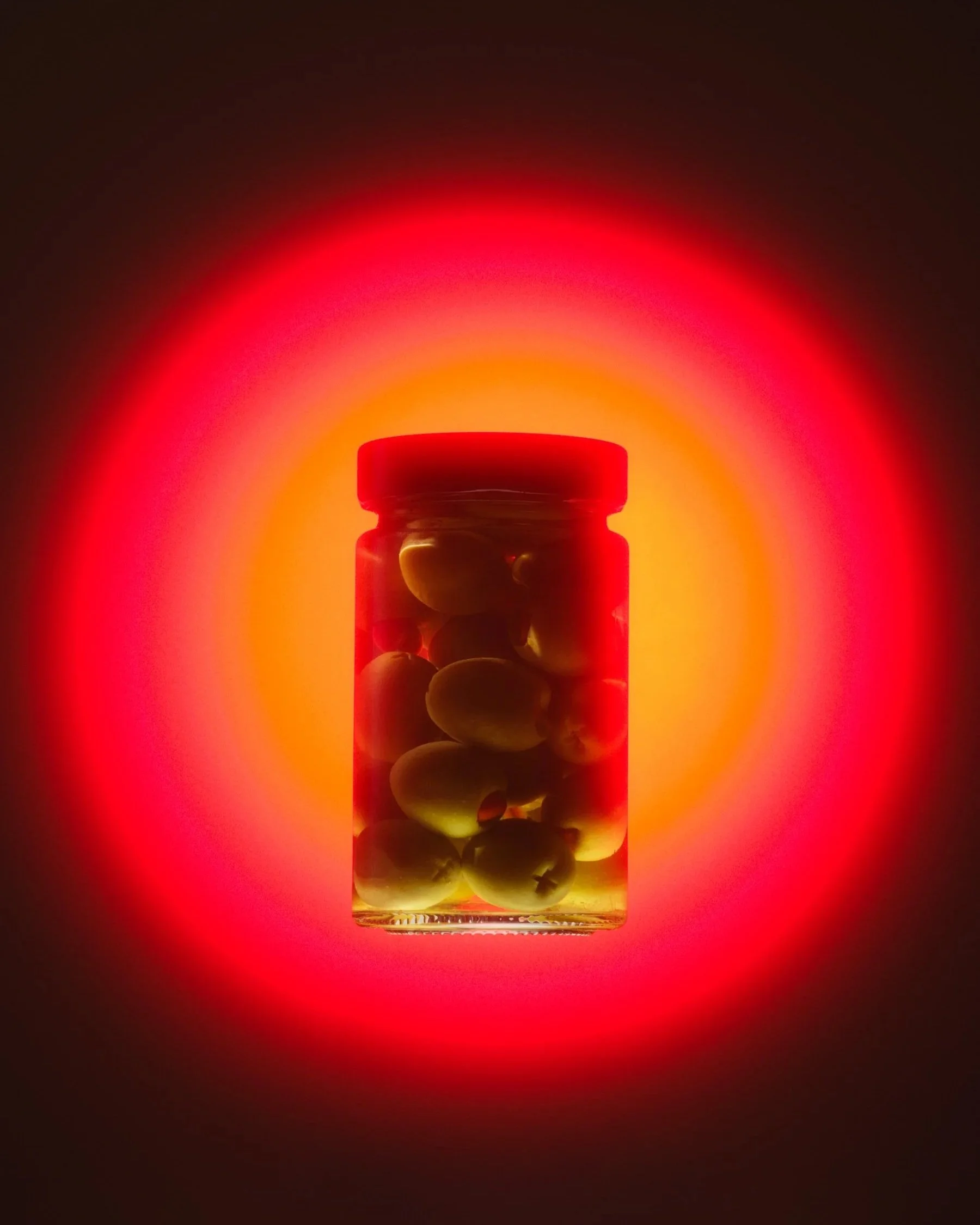 A jar of green olives floats in front of a sphere of glowing red light.