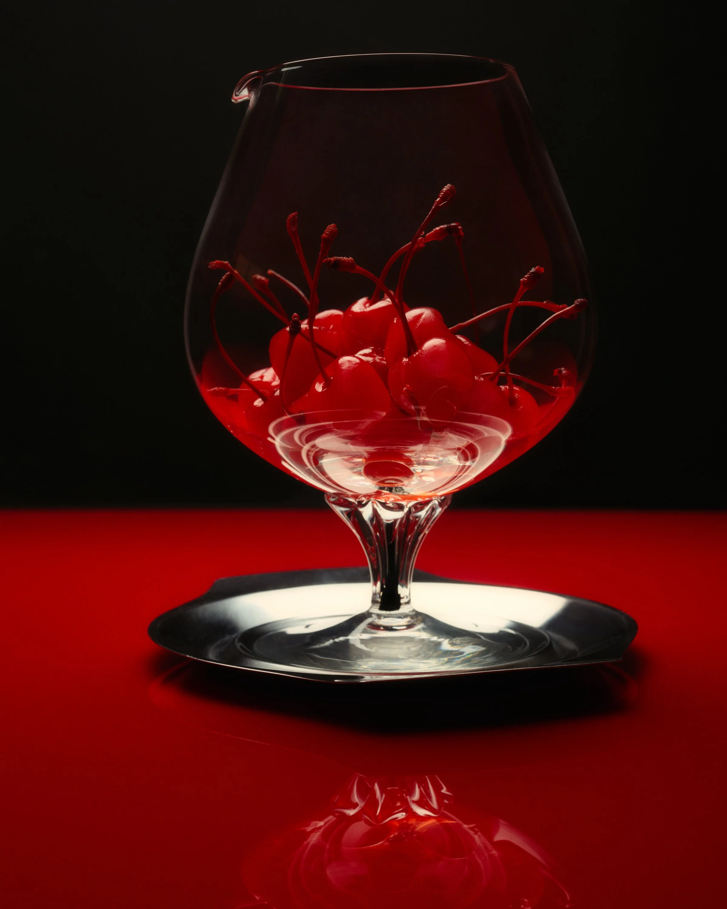 Still life photo of cherries inside a large glass.