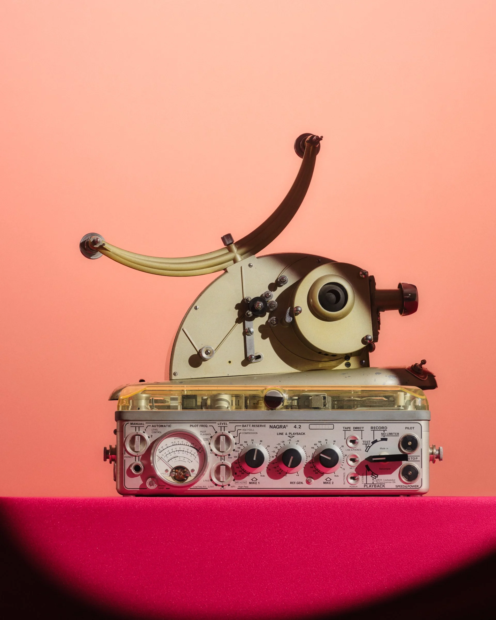 Still life photo of a film projector and radio on a pink background lit with a spotlight.