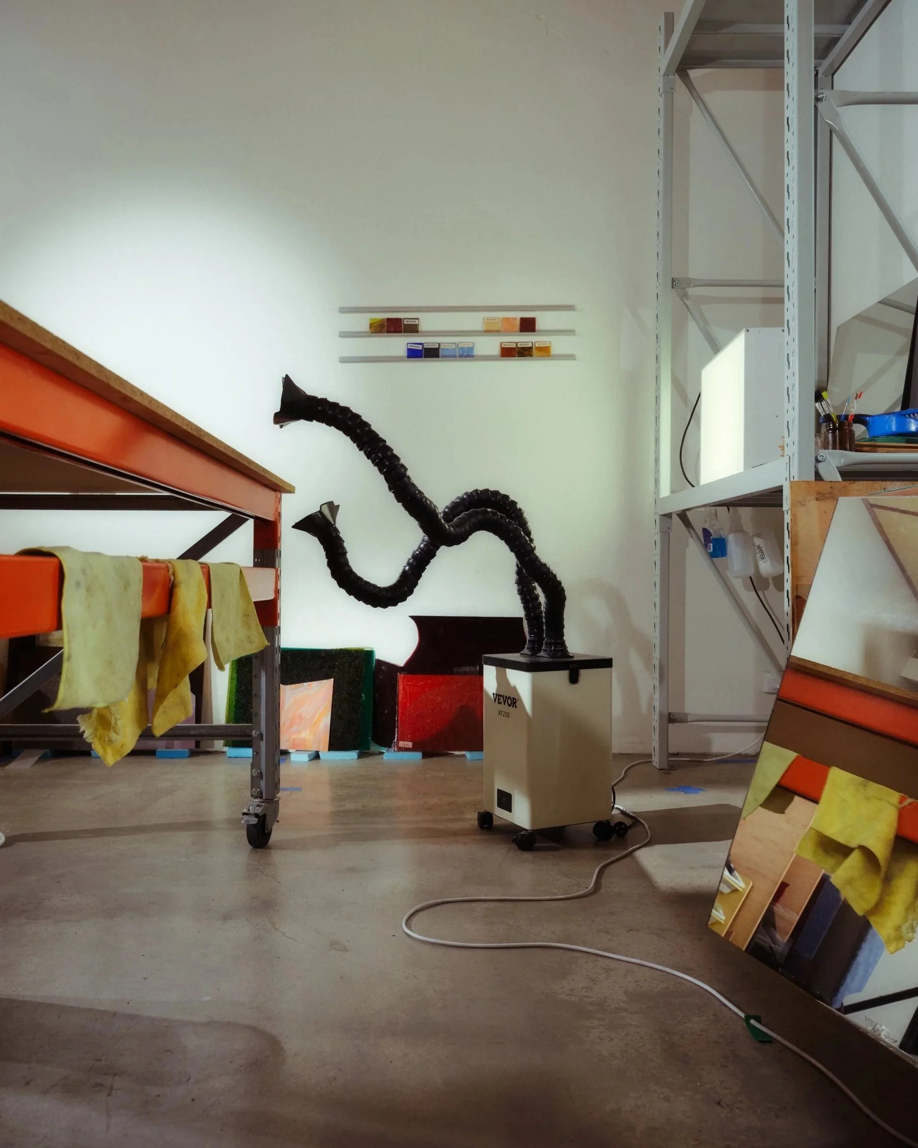 Documentary photo of glass artists Fools Glass studio. Extractor machine extending its arms towards a work bench.