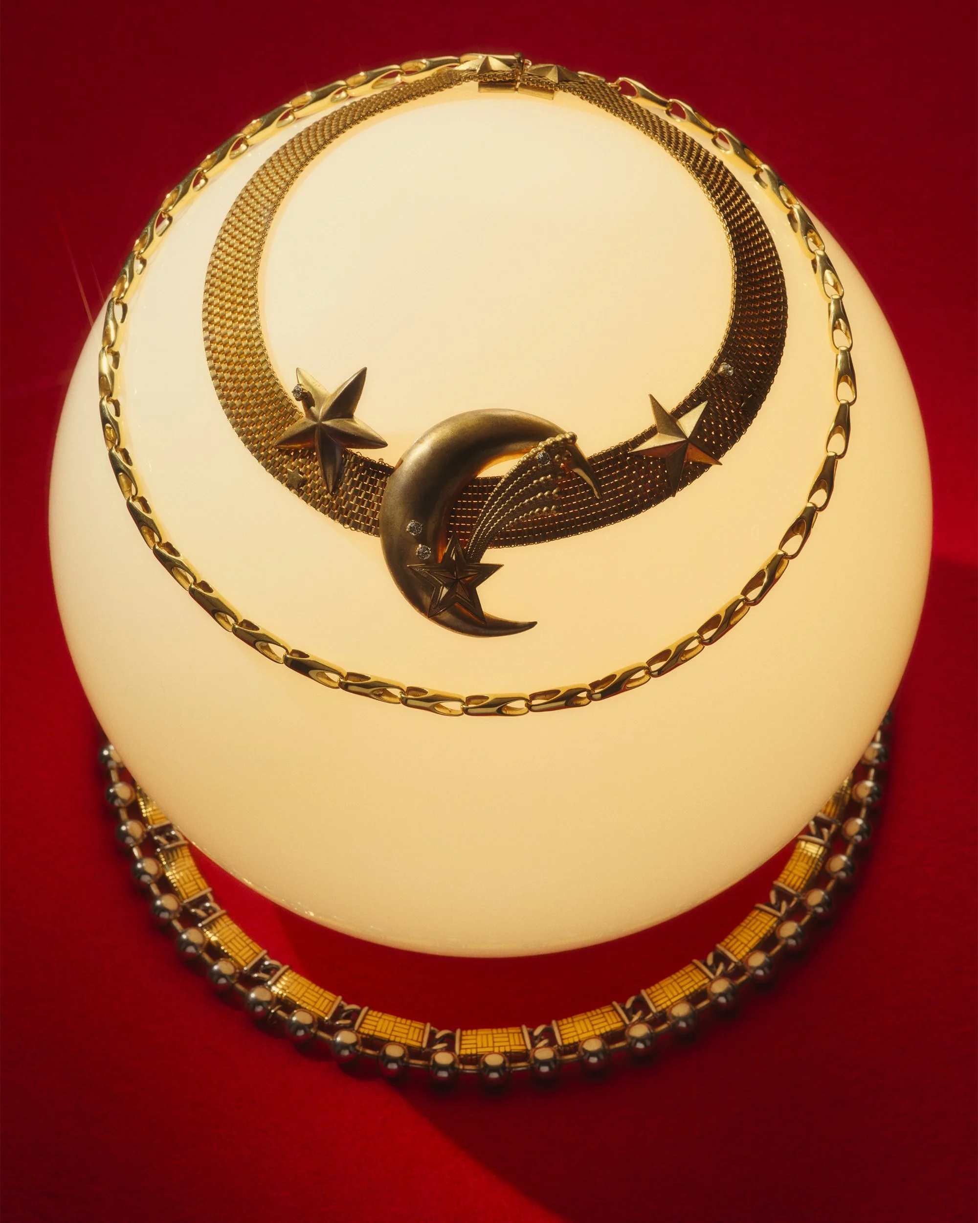 Still Life photo of a glowing sphere layered with gold jewellery chains. The background is red.