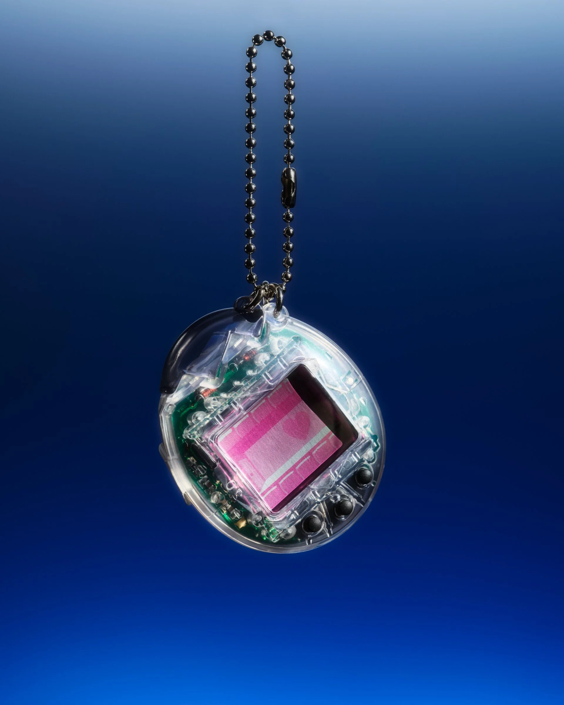 Still life photo of a Tamagotchi floating on a gradient blue background. The case of the Tamagotchi id clear so you can see the circuits inside.