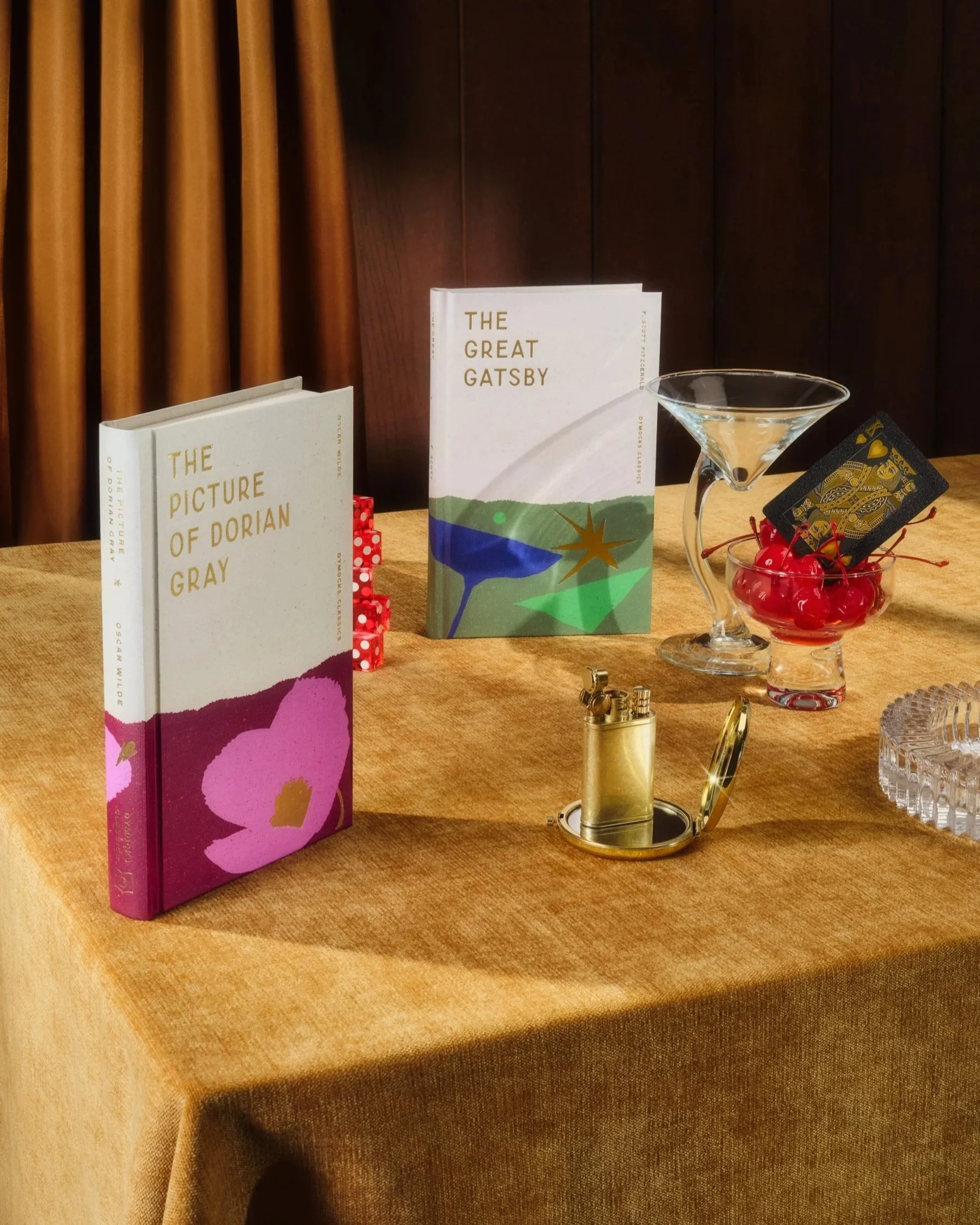 Still life image of two hard cover books in a table setting of glassware and a gold lighter.