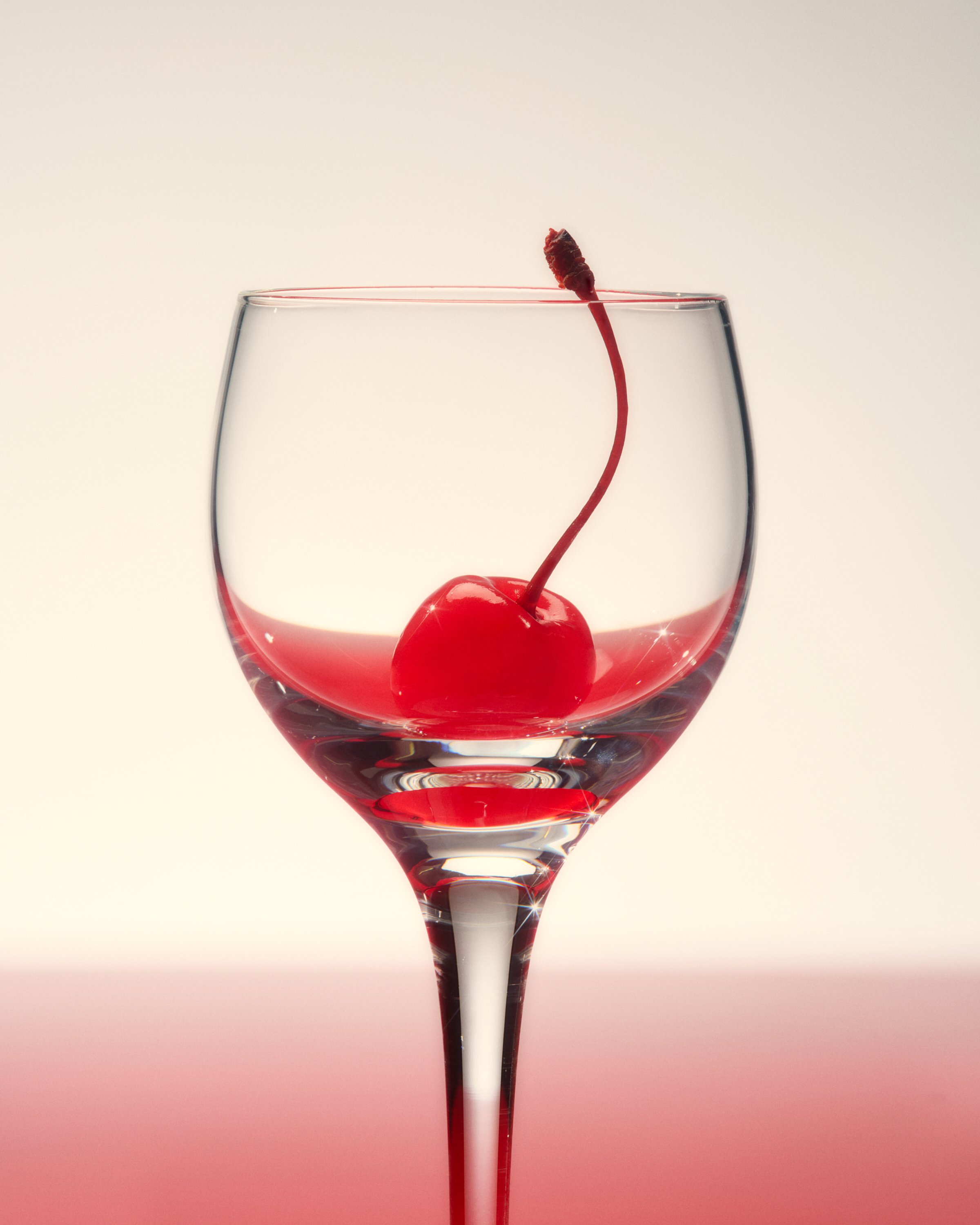 Still life photo of a red cherry inside a glass.