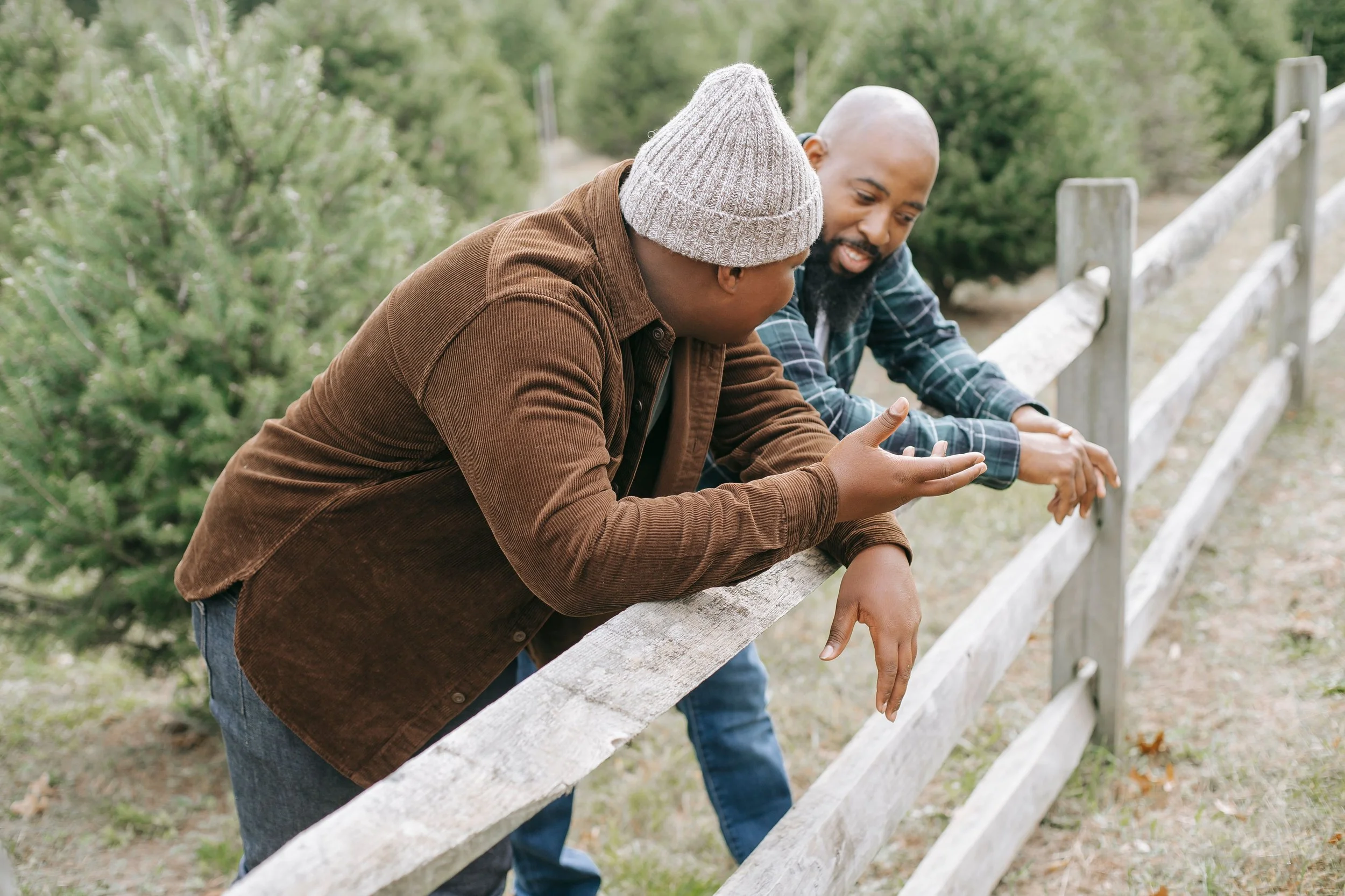 Father and son having a friendly conversation outdoors by a wooden fence.