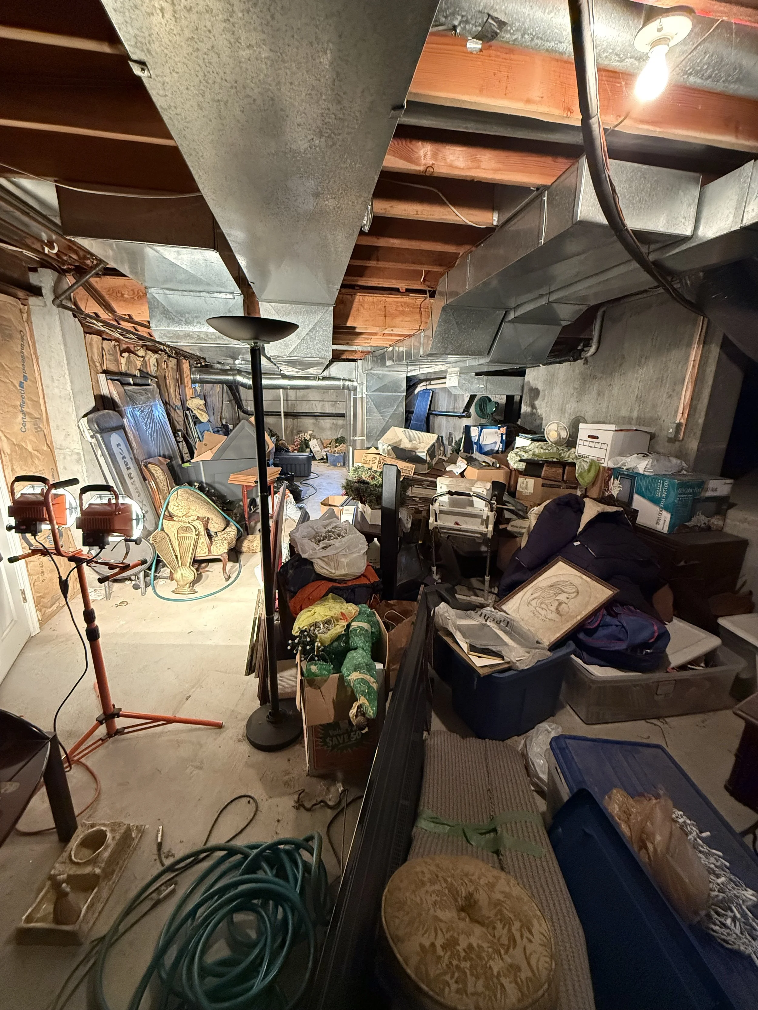 Cluttered basement storage area before professional organizing in Mercer County, Central New Jersey, with piled boxes and scattered household items.