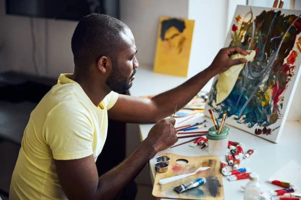 Man in a yellow shirt painting an abstract artwork on a canvas in a well-lit art therapy studio in Philadelphia.