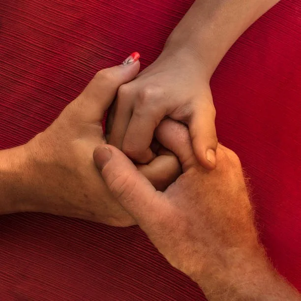 Three adults holding hands with a red surface underneath.