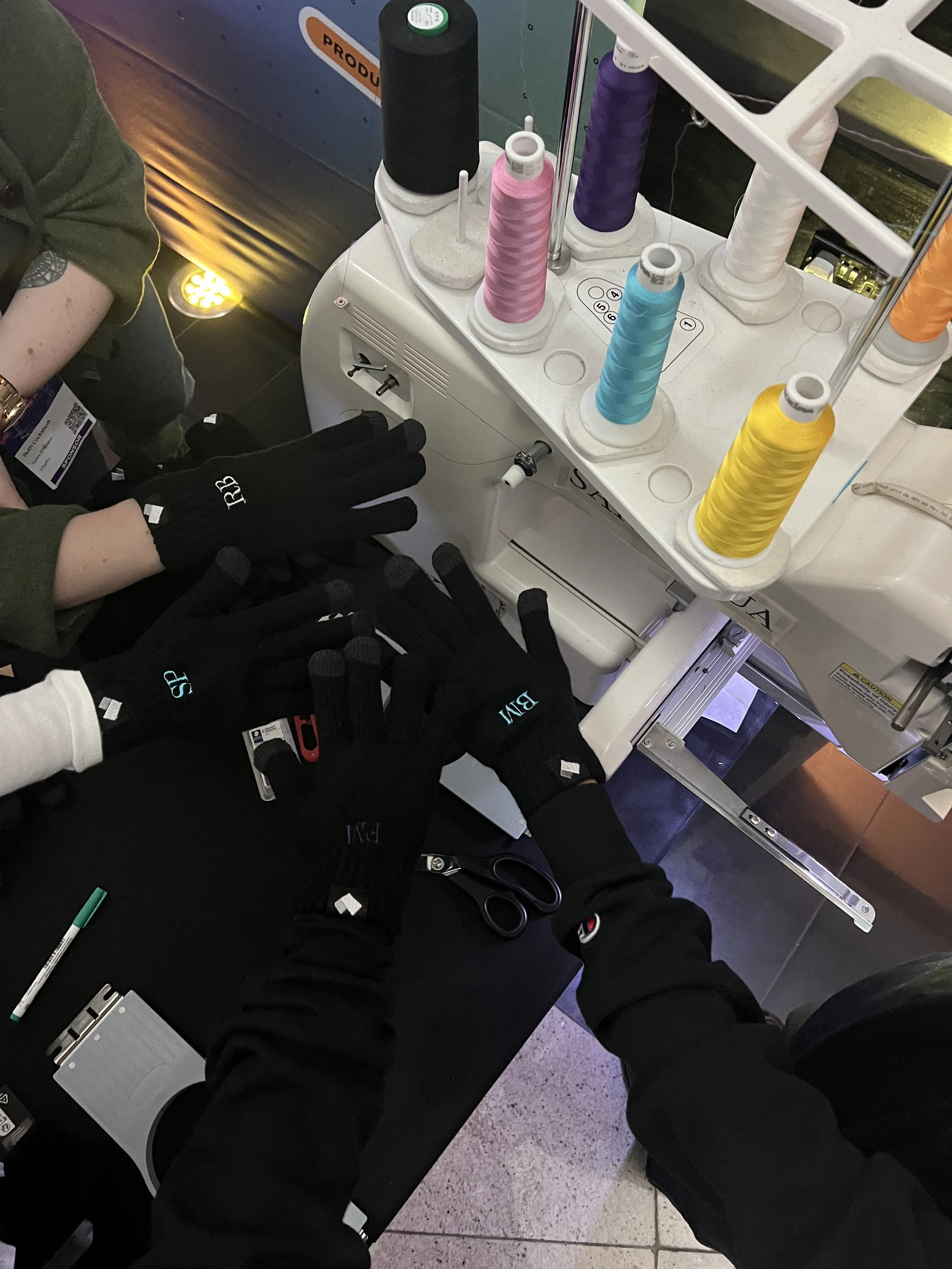Embroidery machine with colorful threads and gloved hands showcasing initials