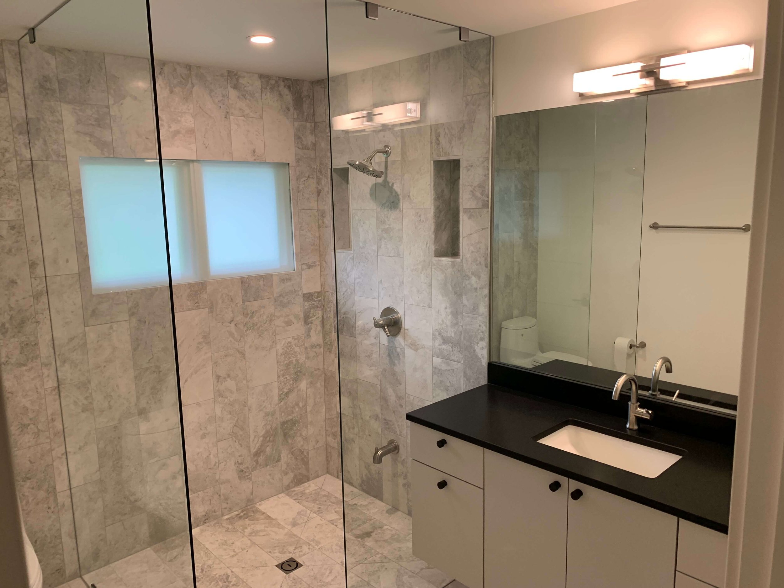 Close-up of a custom walk-in shower with white subway tile, a built-in bench, and matte black fixtures installed by Urbandale contractors.