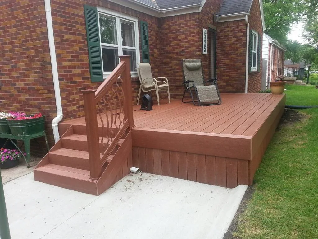 Ground-level composite deck in Des Moines attached to a brick home, featuring integrated steps and decorative railing.