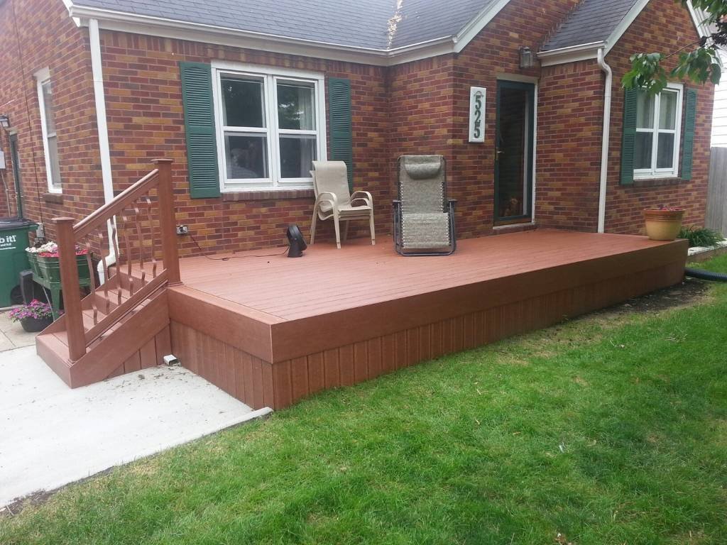 Ground-level composite deck in Des Moines attached to a brick home, featuring stairs with decorative railing and low-maintenance decking boards.