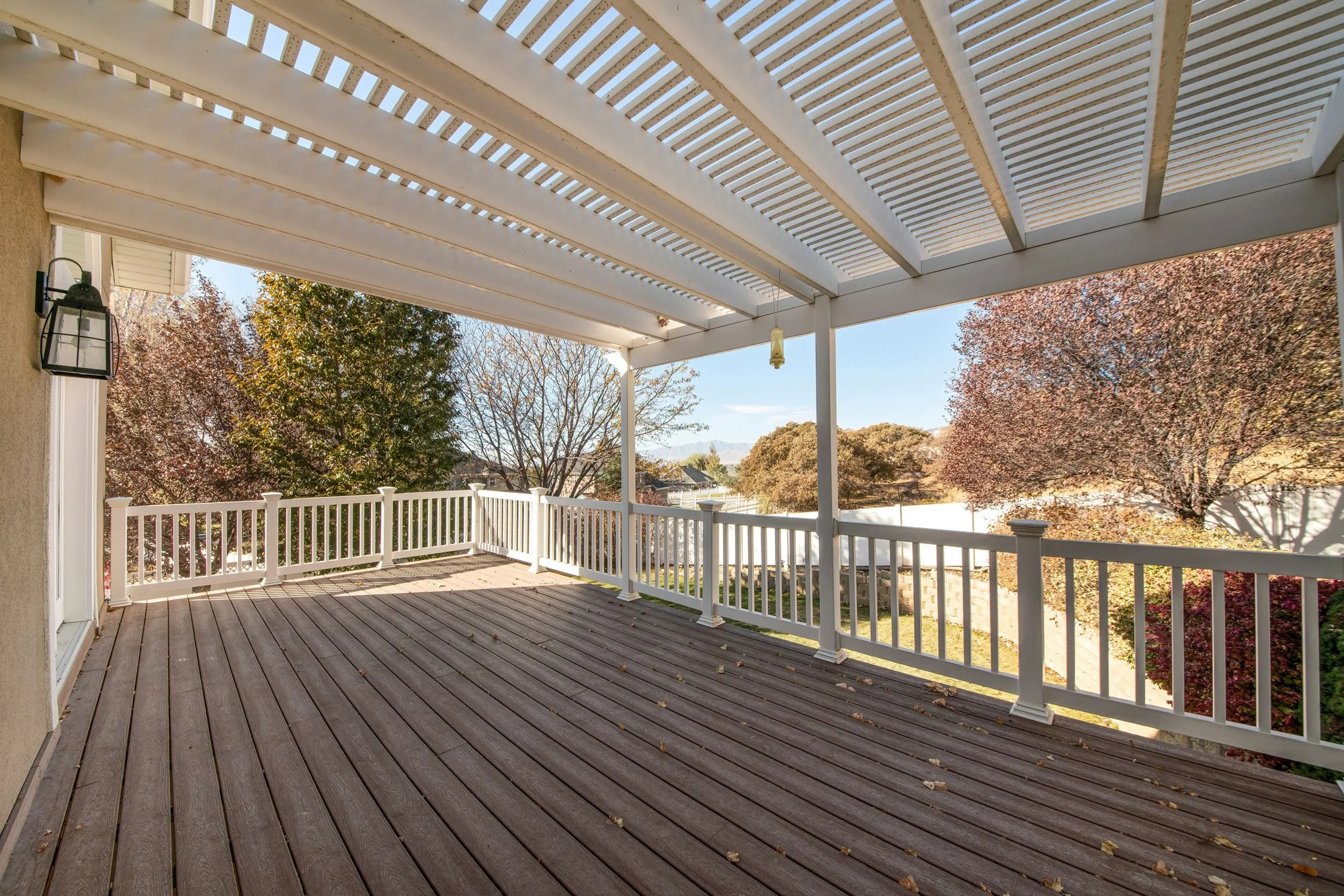 Elevated backyard deck with white pergola structure and railing, creating shaded outdoor living space attached to a home.