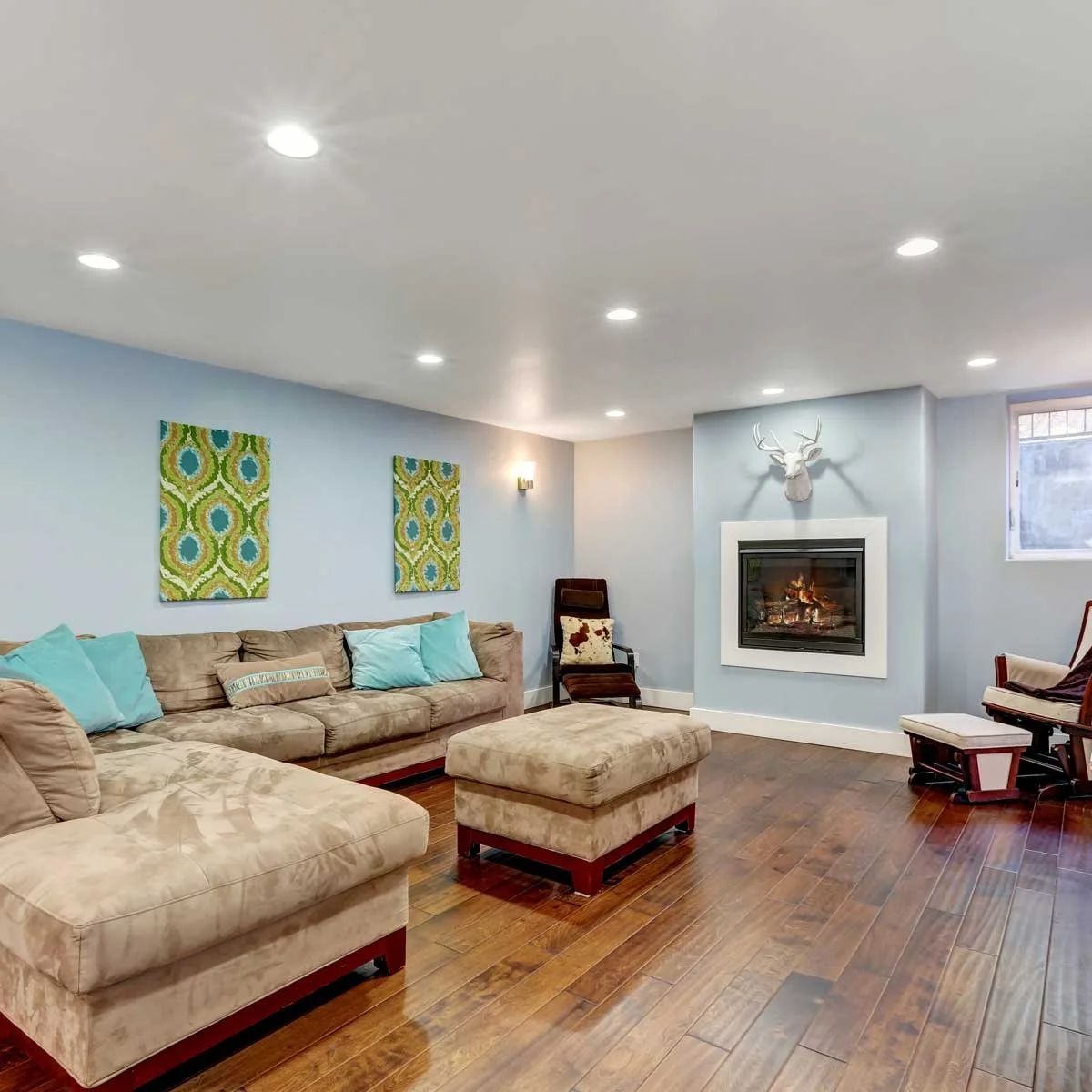 Cozy basement lounge featuring a modern fireplace, light blue walls, dark hardwood floors, and a large tan sectional sofa.