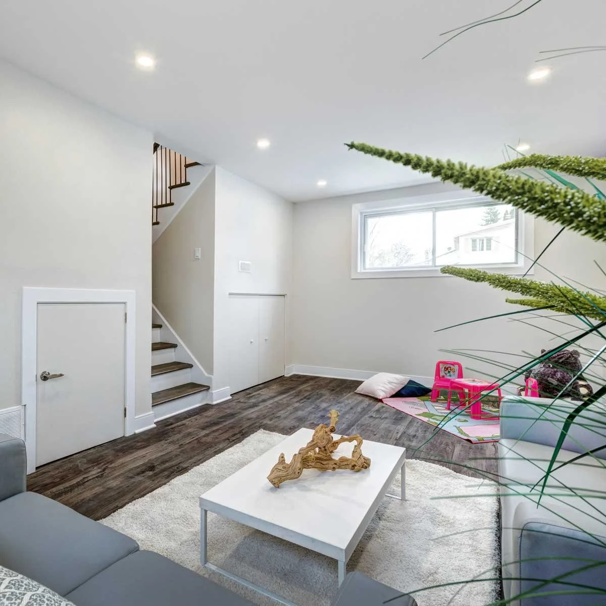 Finished basement in Des Moines with a modern family room layout, light gray walls, dark wood-look flooring, and a children's play area.