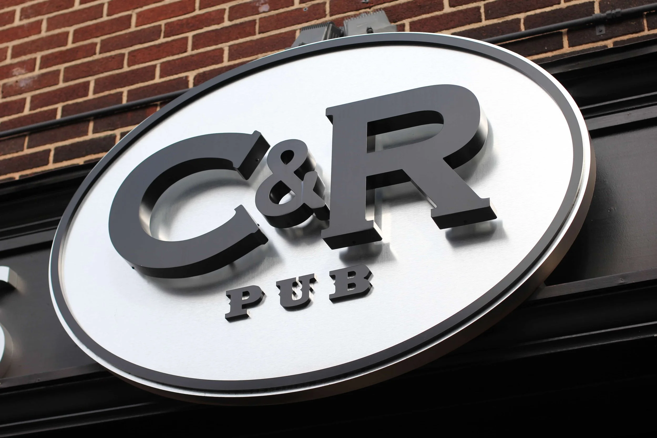 Sign for a C&R Pub mounted on a building's exterior brick wall.