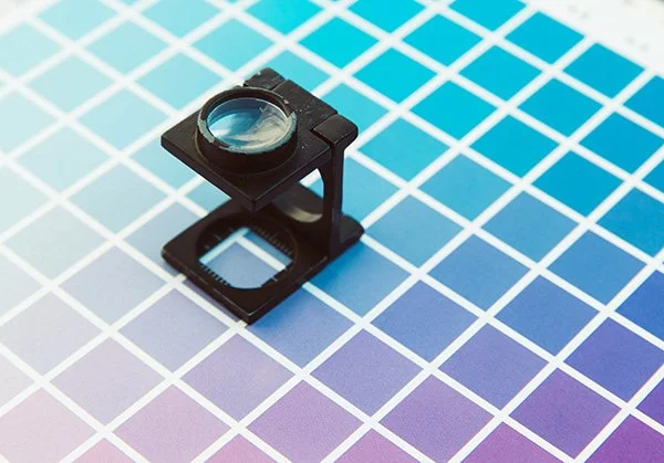A camera lens test chart with a magnifying glass on a colorful grid background